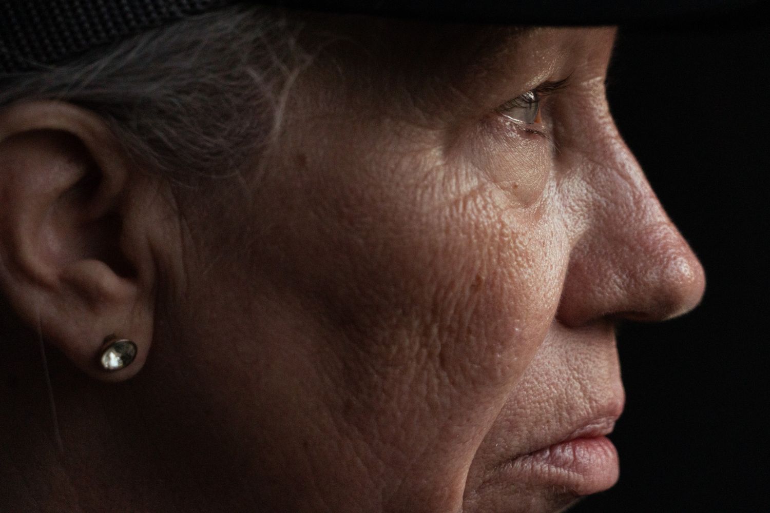 Close-up profile view shows textured skin and earring in dramatic lighting.