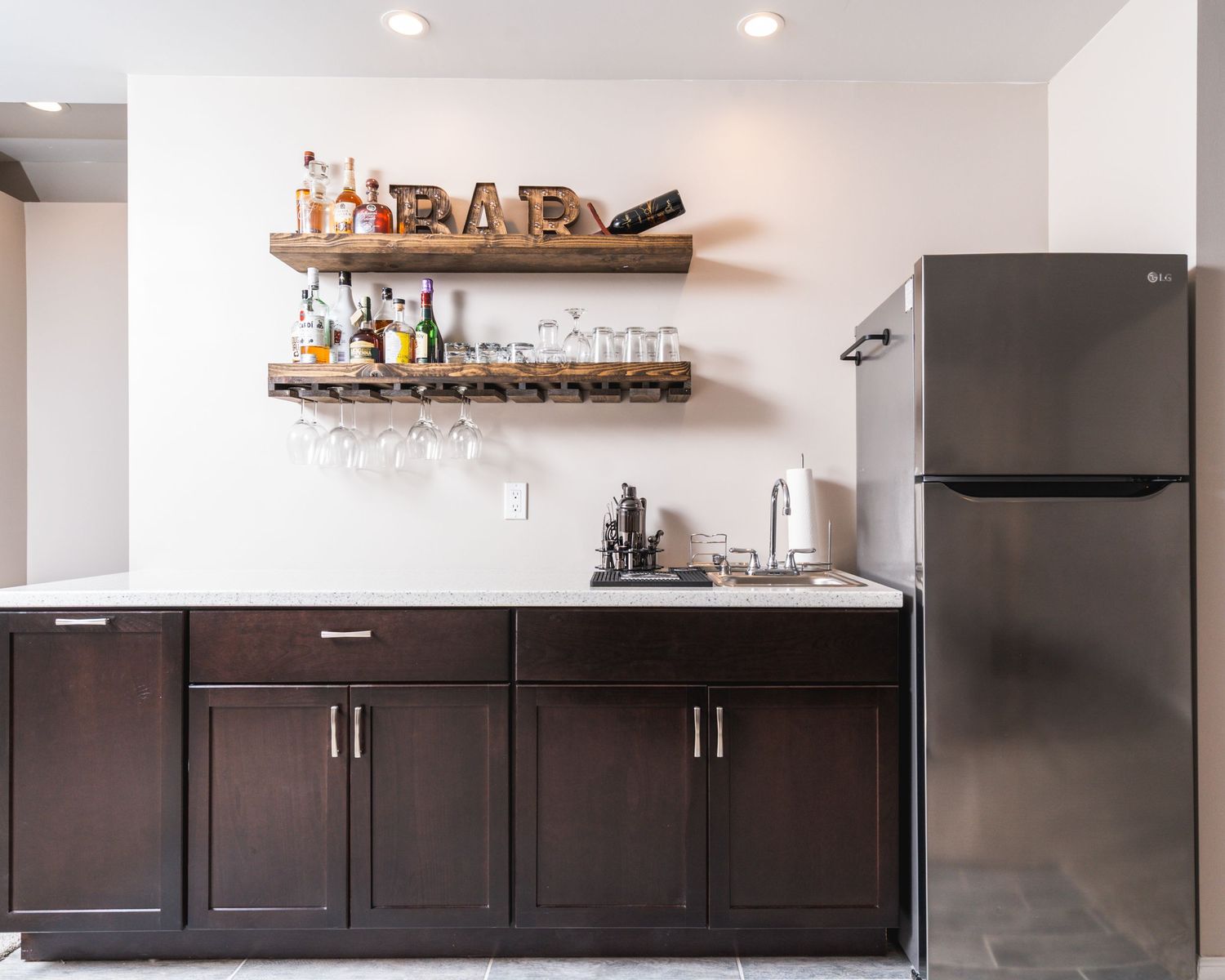 Modern kitchen with dark brown cabinets, stainless steel appliances, and floating wood shelves mounted on white walls.