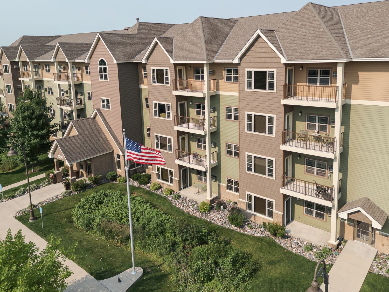 Aerial view of a modern multi-story apartment complex with balconies, American flag, and landscaped grounds.