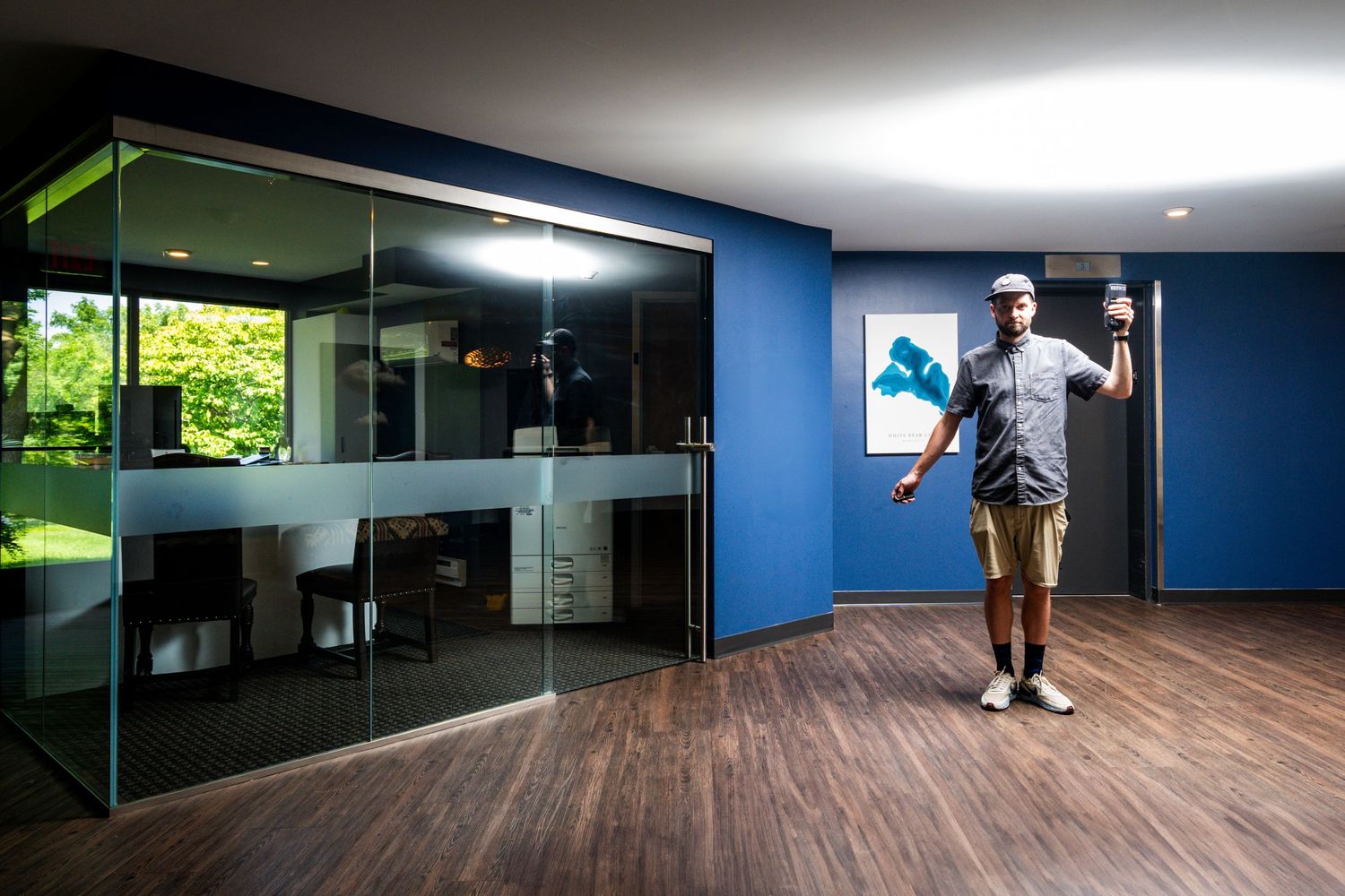 Person standing in a modern office space with blue walls, hardwood floors, and glass partitions.