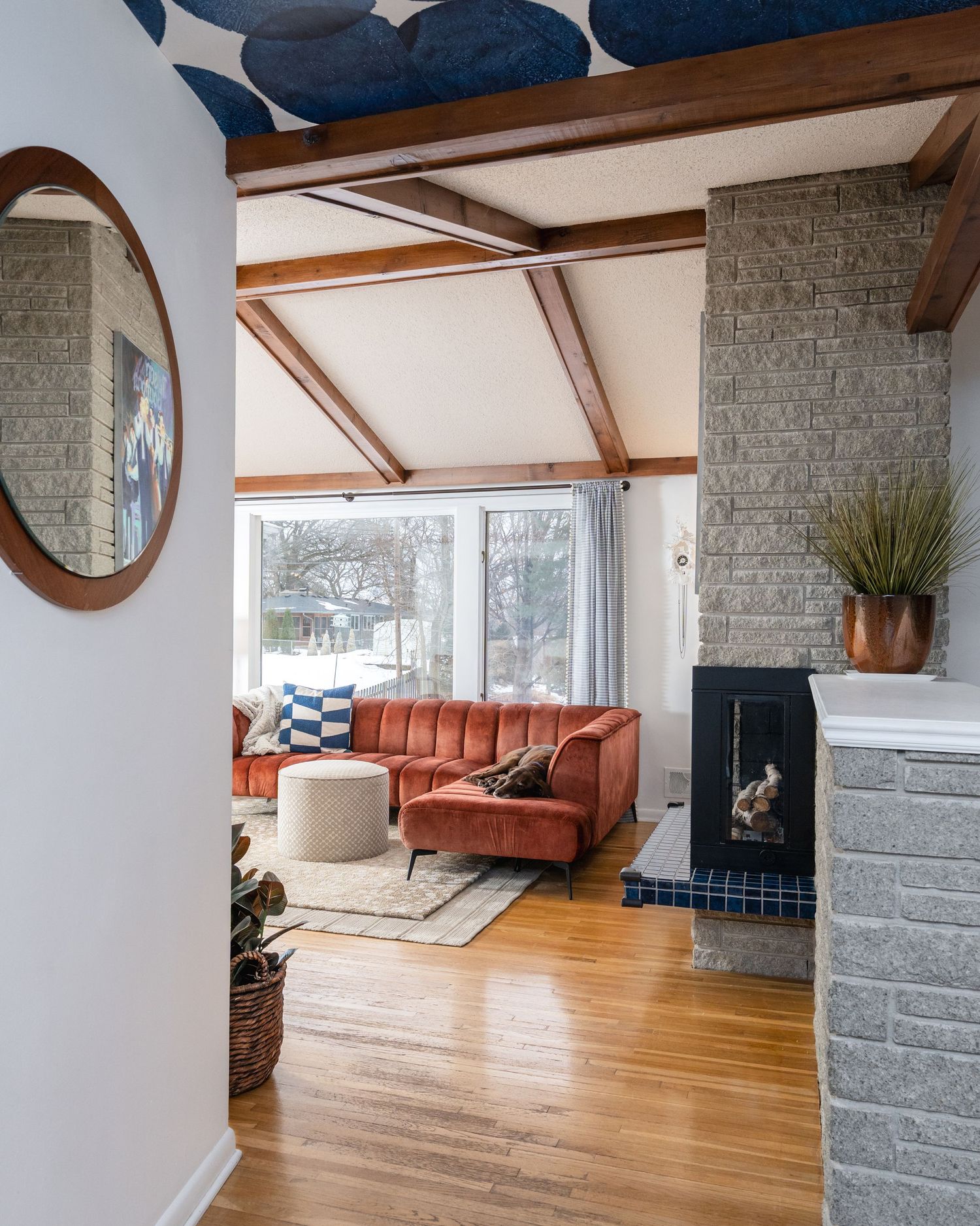 Modern open concept living room with hardwood floors, exposed beams, and a stone fireplace in a mid-century home.