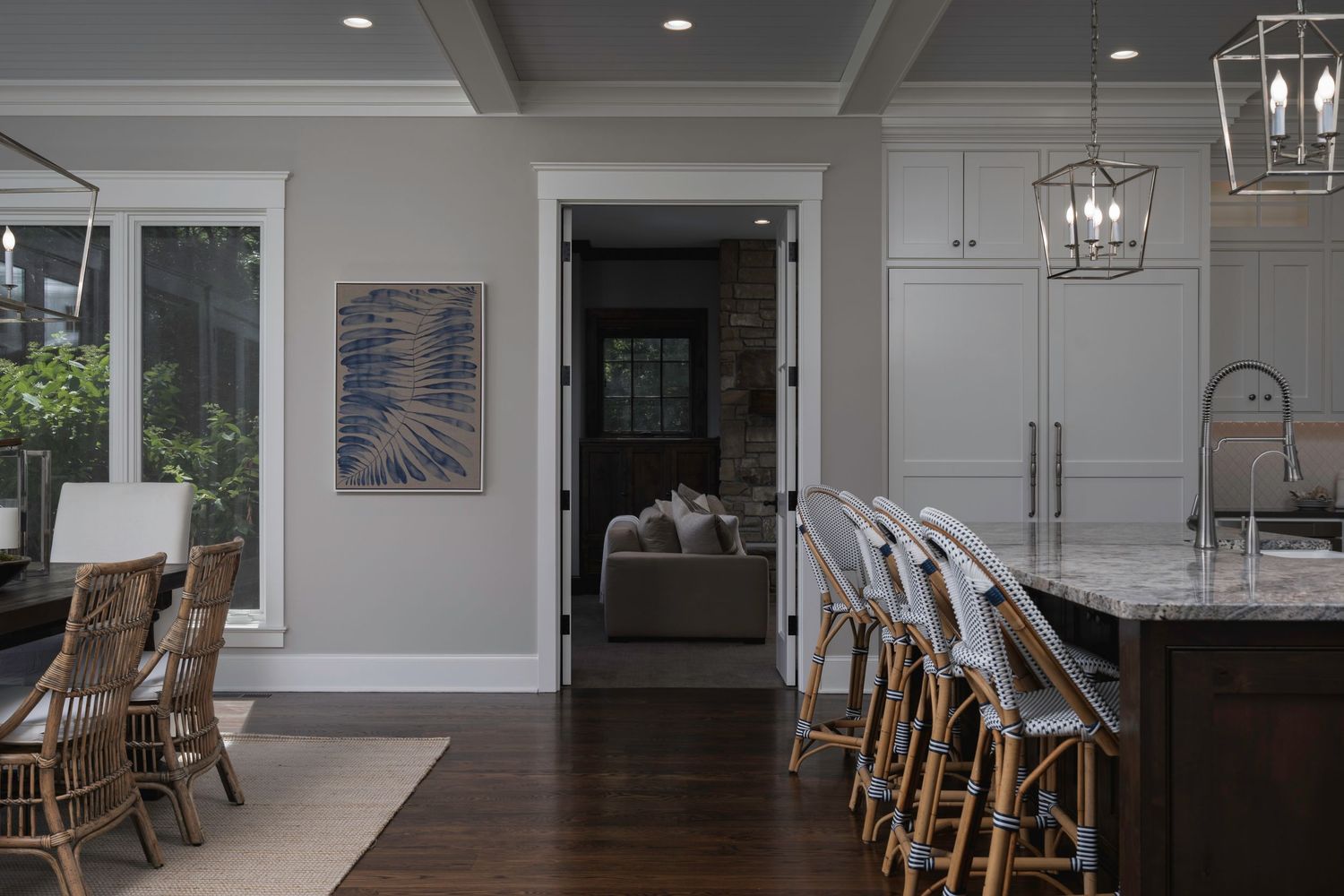 Open-concept kitchen and dining area with dark island, wicker bar stools, hardwood floors, and elegant pendant lighting.