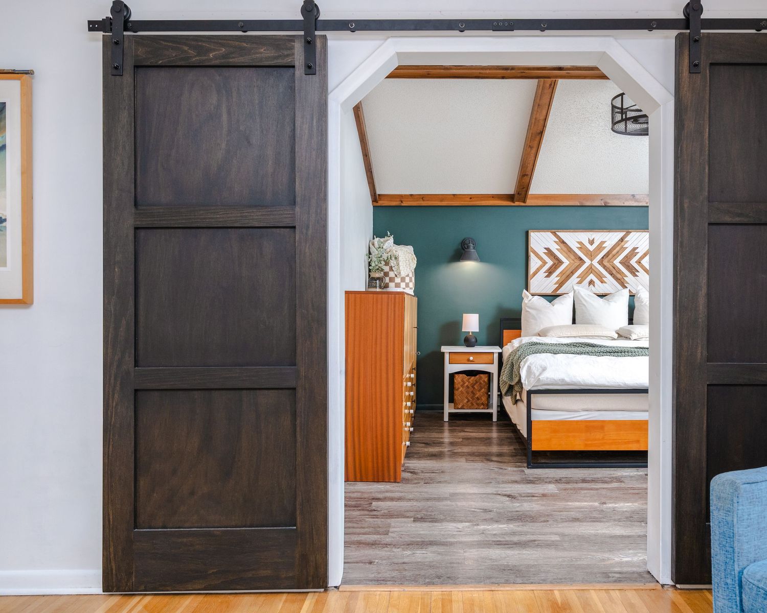 Modern black sliding barn door hardware mounted on white wall with hardwood floors and teal accent wall.