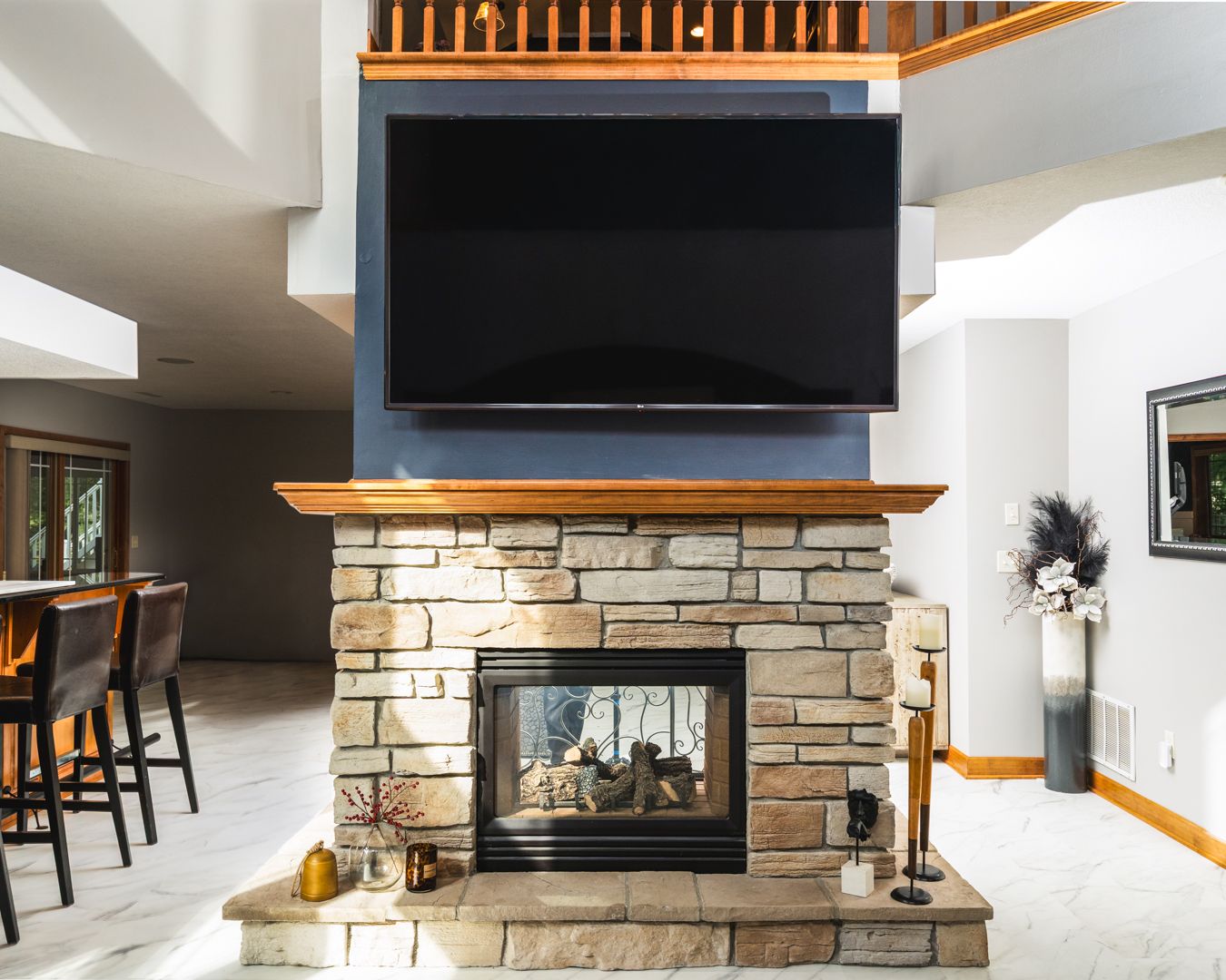 Modern living room features stone fireplace, wood railings, and sleek design elements with black TV mounted above hearth.