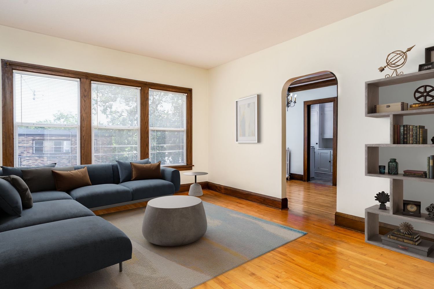 Modern living room with gray sectional sofa, wood floors, large windows, and built-in shelving in a bright space.