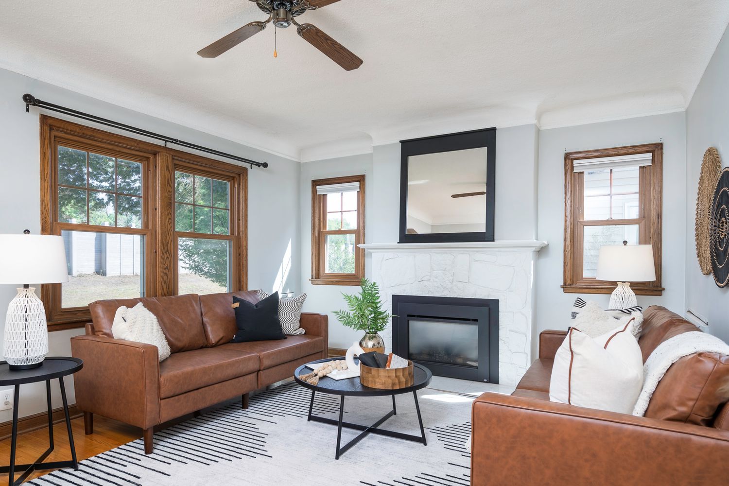 Bright living room with brown leather sofas, fireplace, striped rug, and wood-trimmed windows in a modern home.