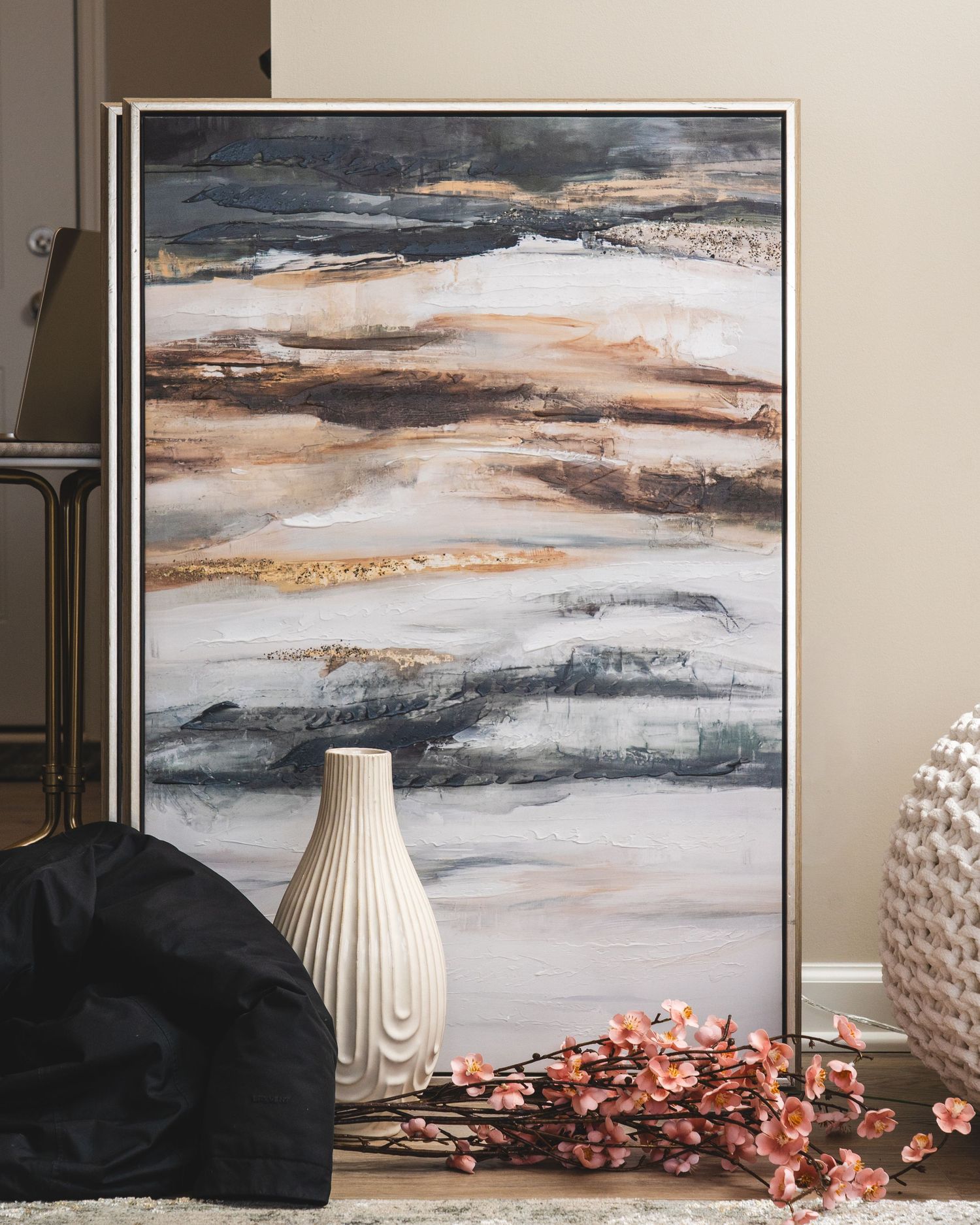 Modern abstract landscape artwork in gray and copper tones displayed above white ceramic vases on a console table.