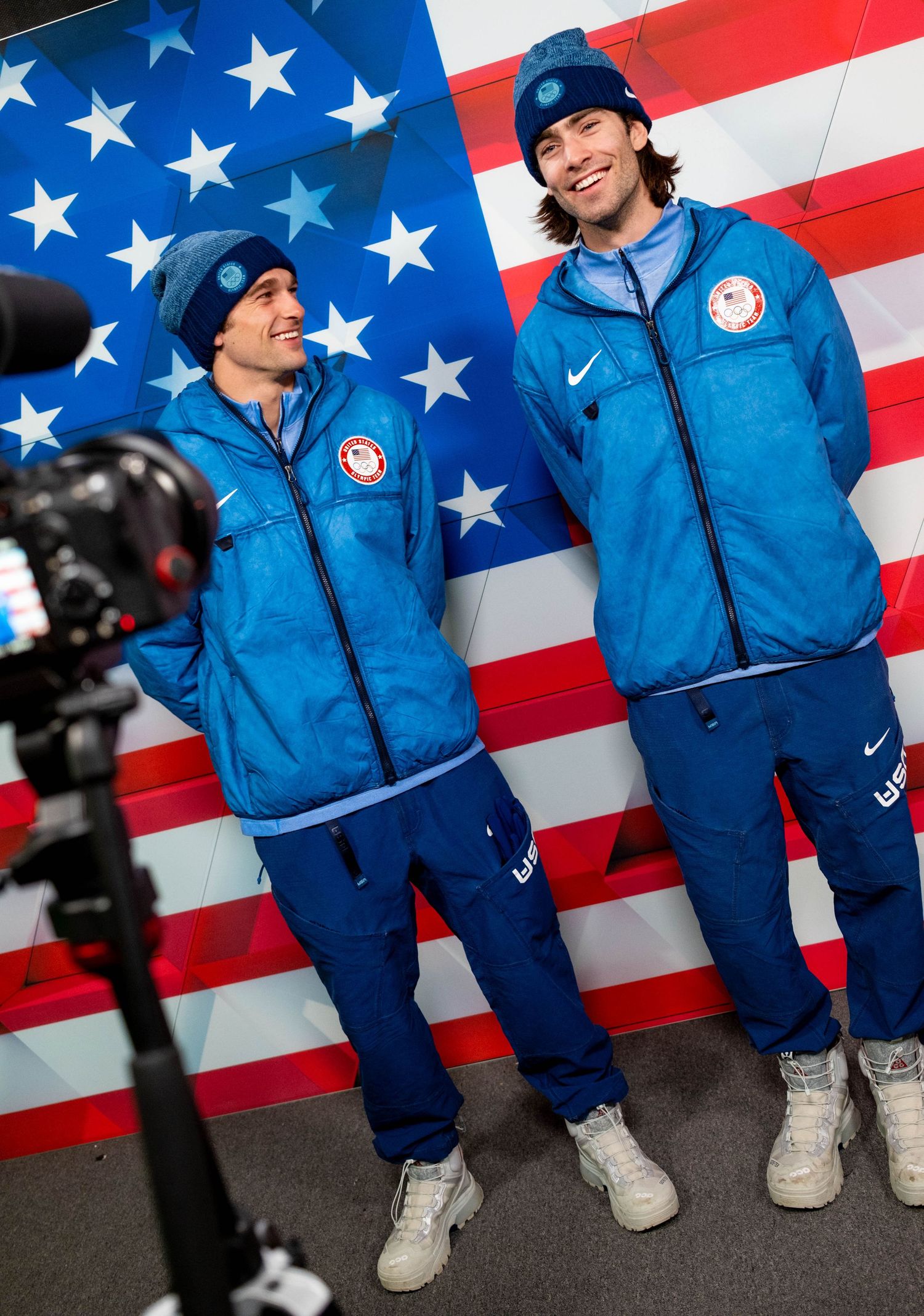 Two athletes in Team USA uniforms posing in front of American flag during photo shoot.