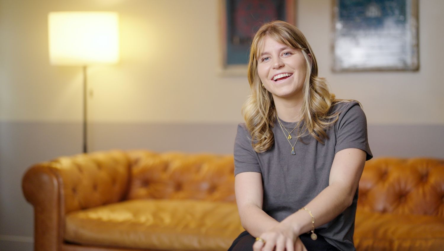 Person sitting on orange couch smiles during indoor interview setting.