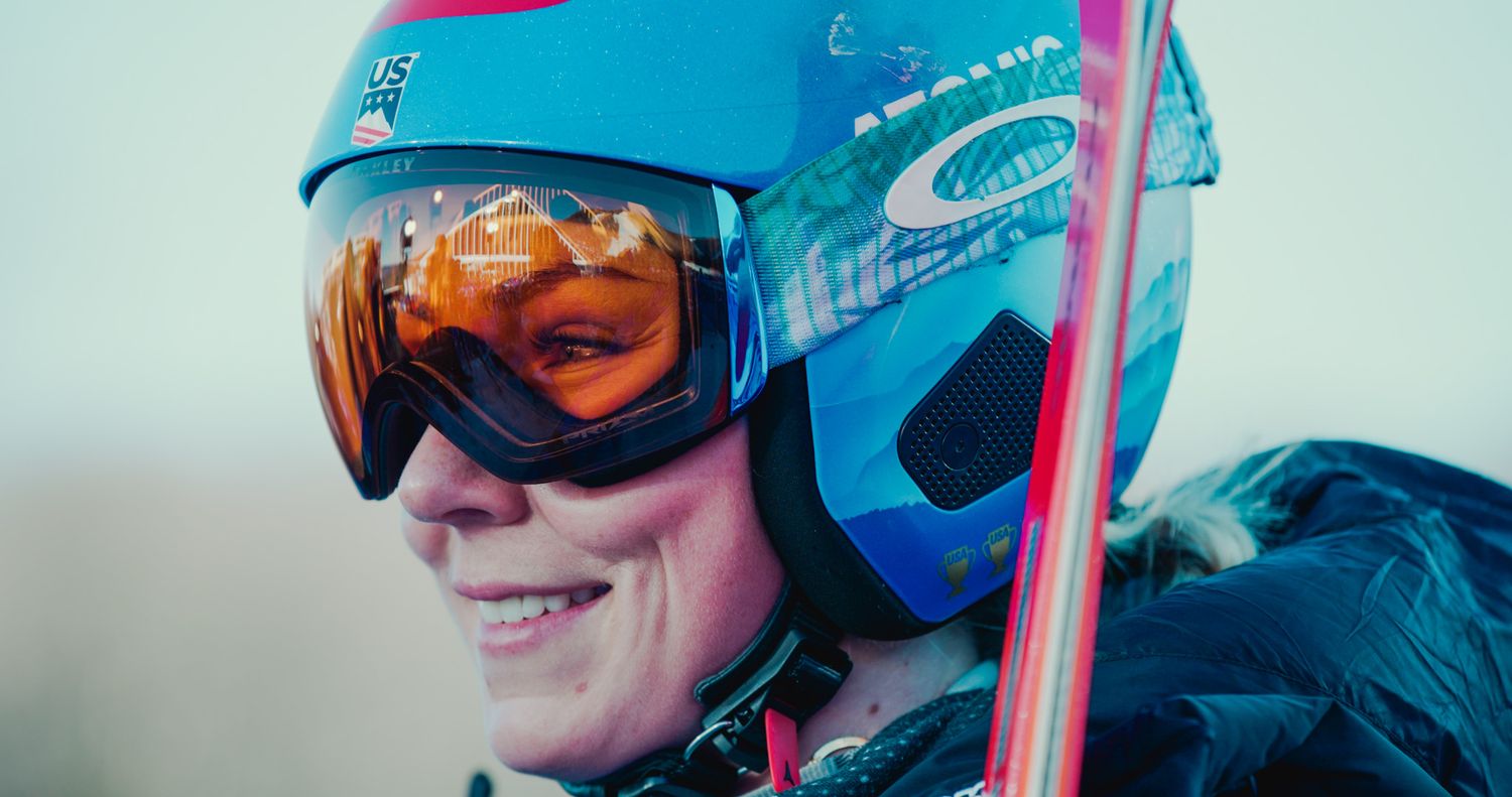 Skier wearing blue helmet and reflective goggles smiles while enjoying winter sports.