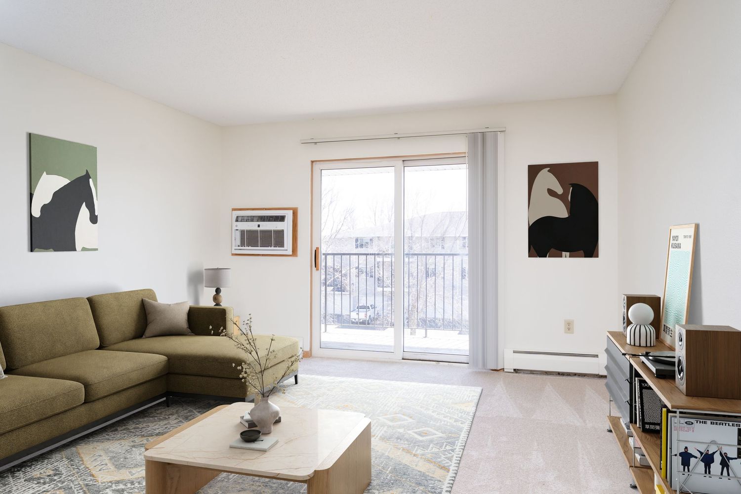 Bright living room with green sofa, coffee table, patterned rug, and sliding glass door leading to a balcony.