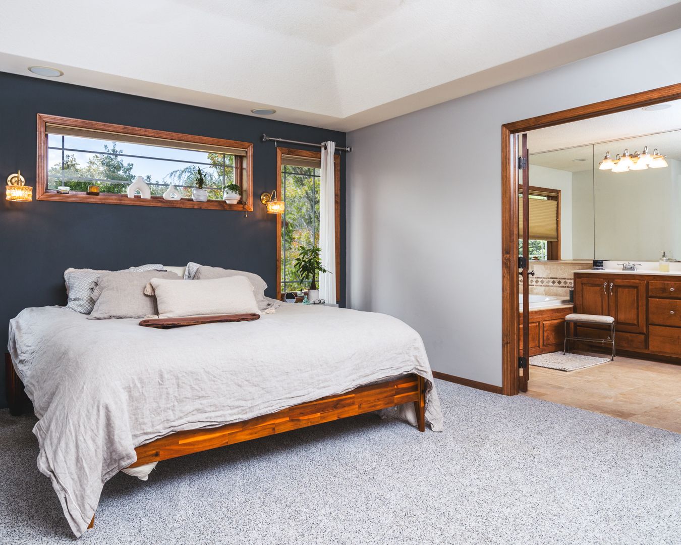 Wide angle view showing multiple angles of a modern bedroom with white carpet, wooden bed frame, and natural lighting.