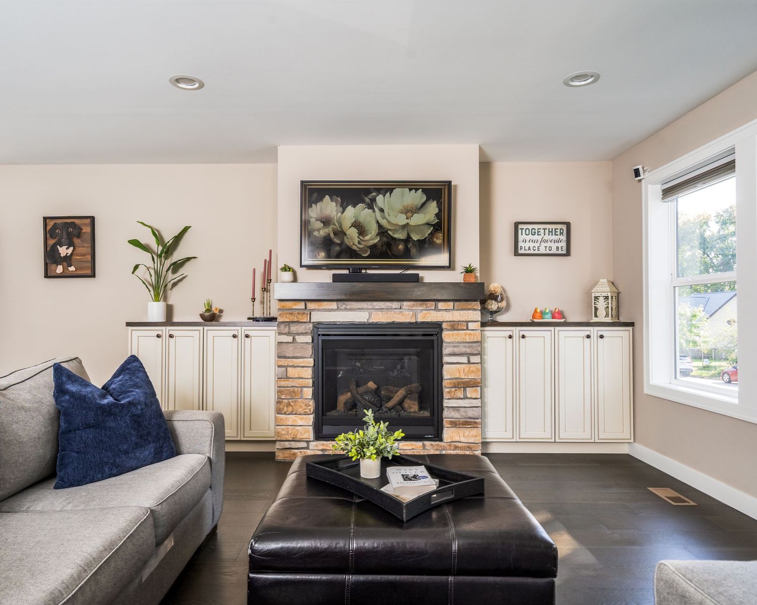 Modern living room features brick fireplace, hardwood floors, and white shiplap walls with natural light streaming through windows.