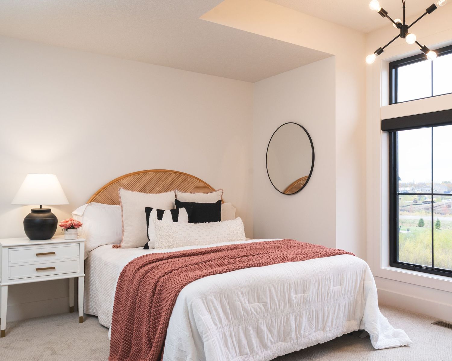 Modern bedroom interior with white bedding, coral throw blanket, and large windows offering natural light.