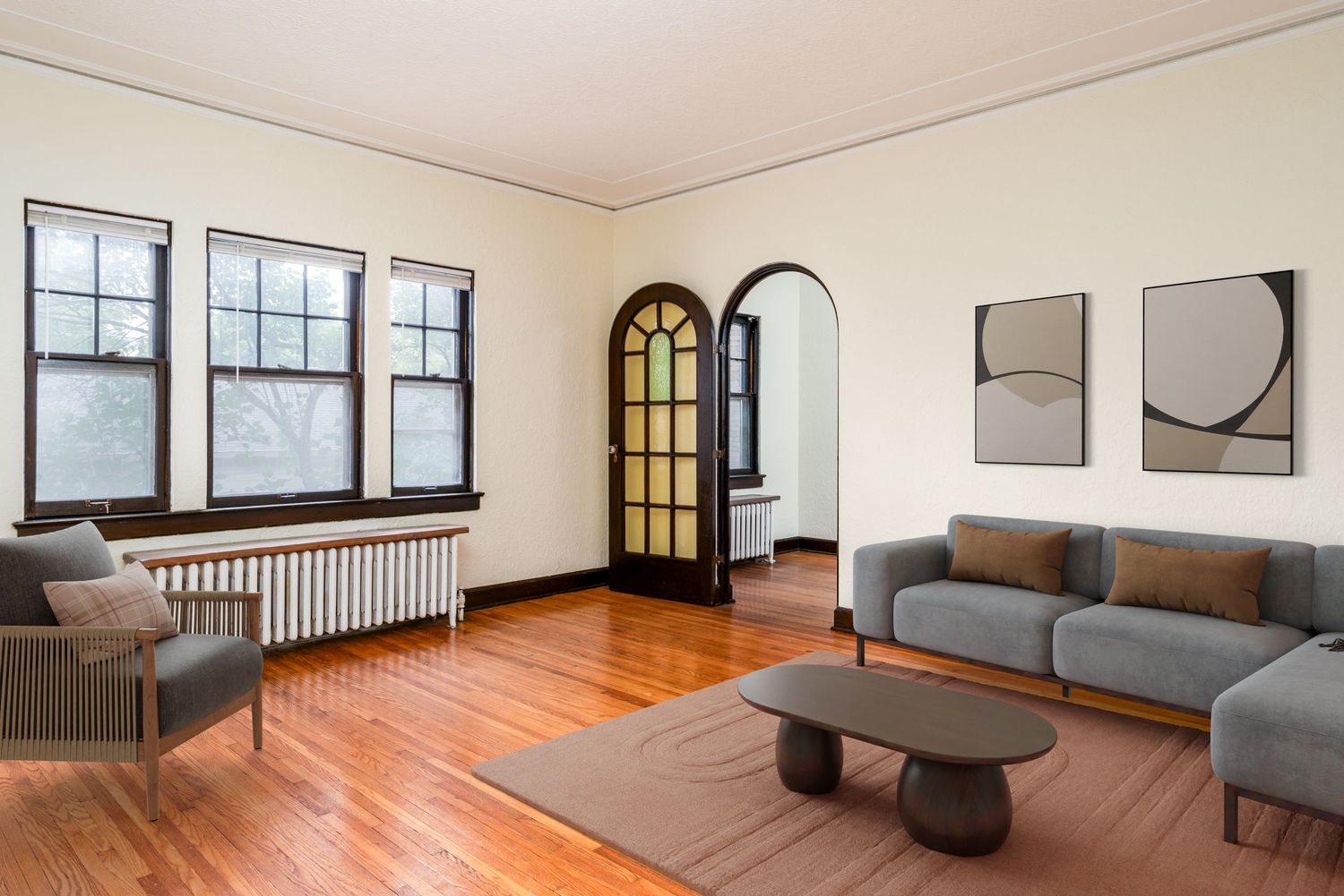 Modern living room with hardwood floors, arched doorway, gray sectional sofa, and minimalist black and white wall art.
