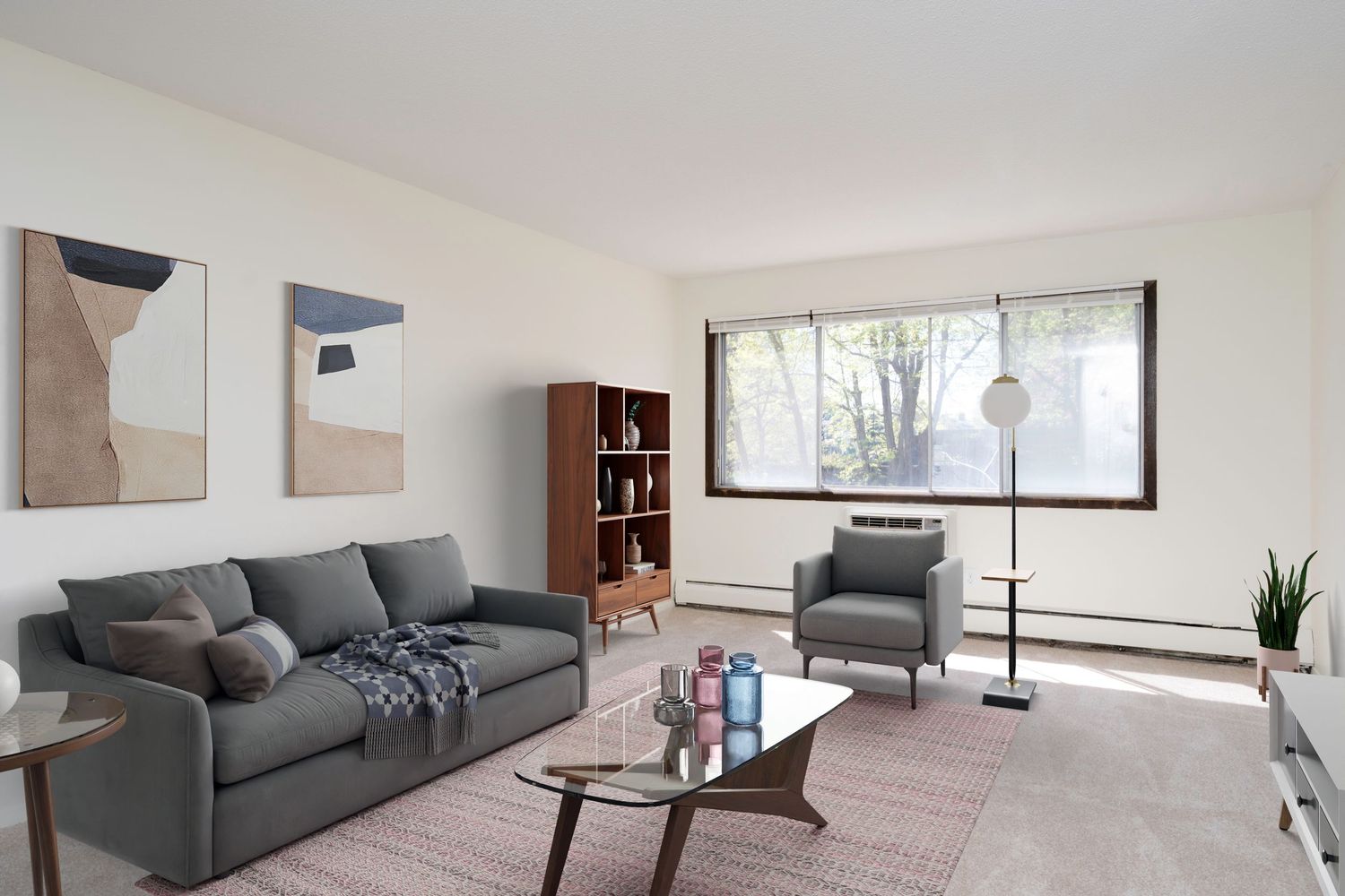 Modern living room with gray sofa, mid-century armchair, wood bookcase, and large window overlooking trees.