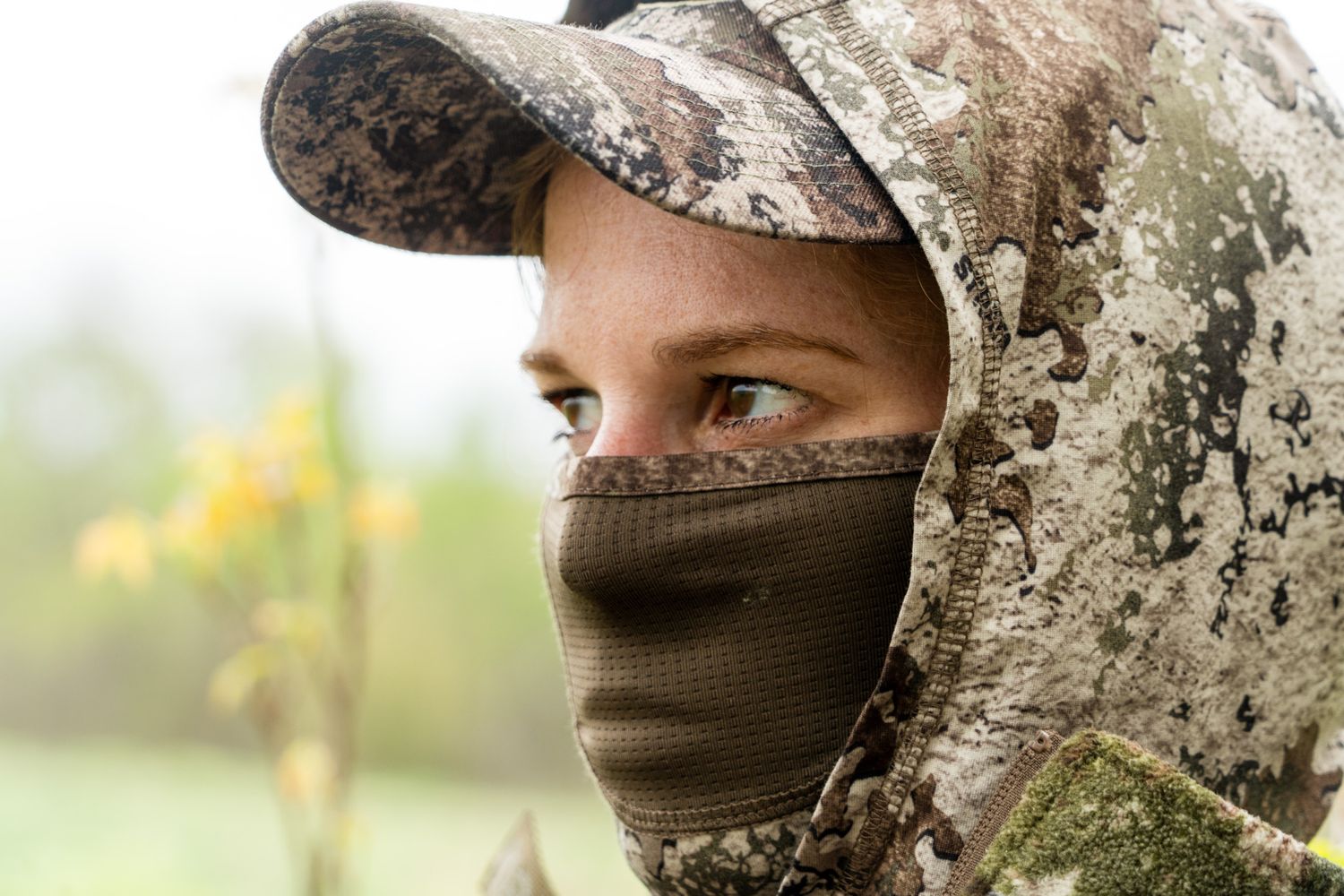 Close-up of a hunter wearing camouflage and face mask in an outdoor setting.