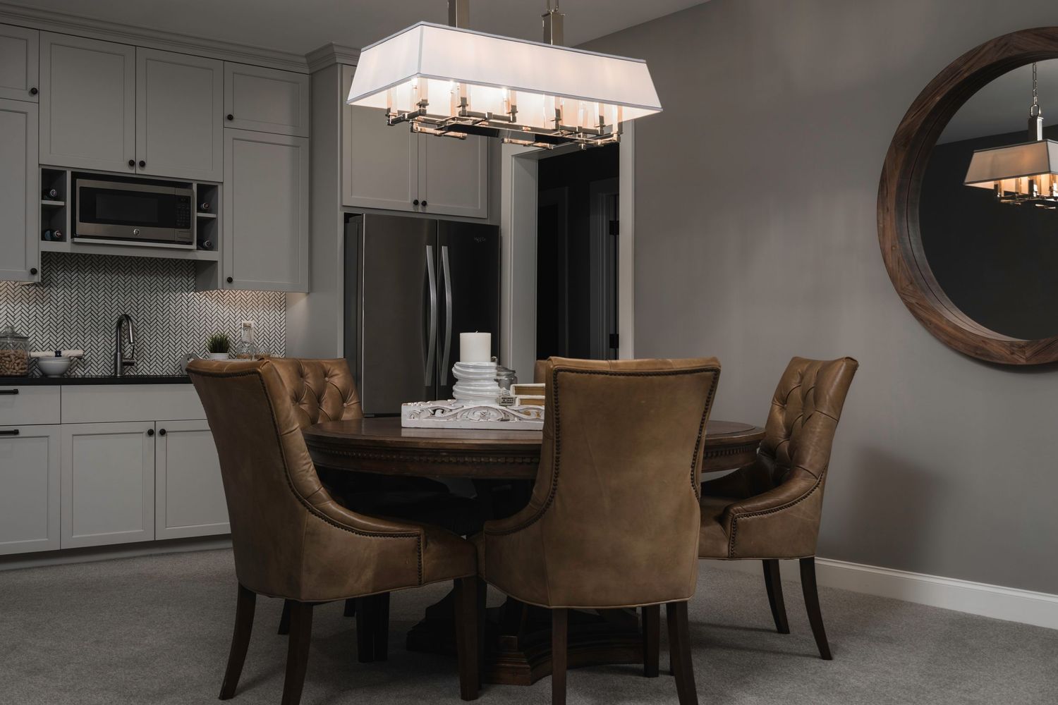 Elegant dining room with round wooden table, brown upholstered chairs, white cabinetry, and a rectangular pendant light.