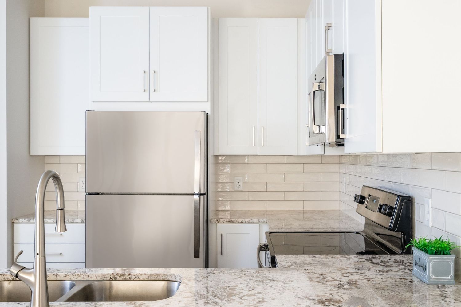 Modern white kitchen interior with marble countertops, stainless steel appliances and bright natural lighting.