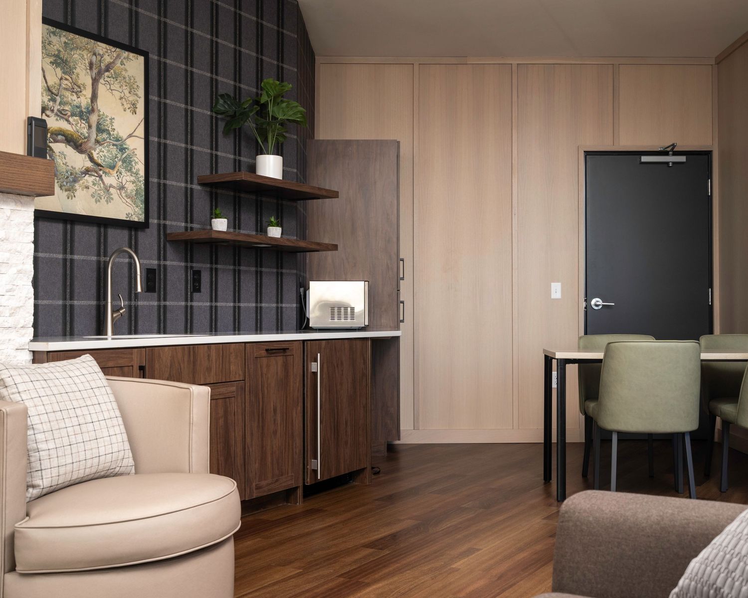 Modern studio apartment featuring a kitchenette with dark tile backsplash, wood cabinets, open shelving, and dining area near a dark door.