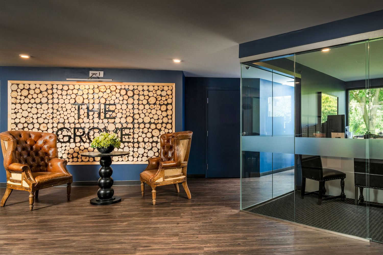 Modern office lobby features leather wingback chairs and decorative wood block wall art next to glass-walled meeting room.
