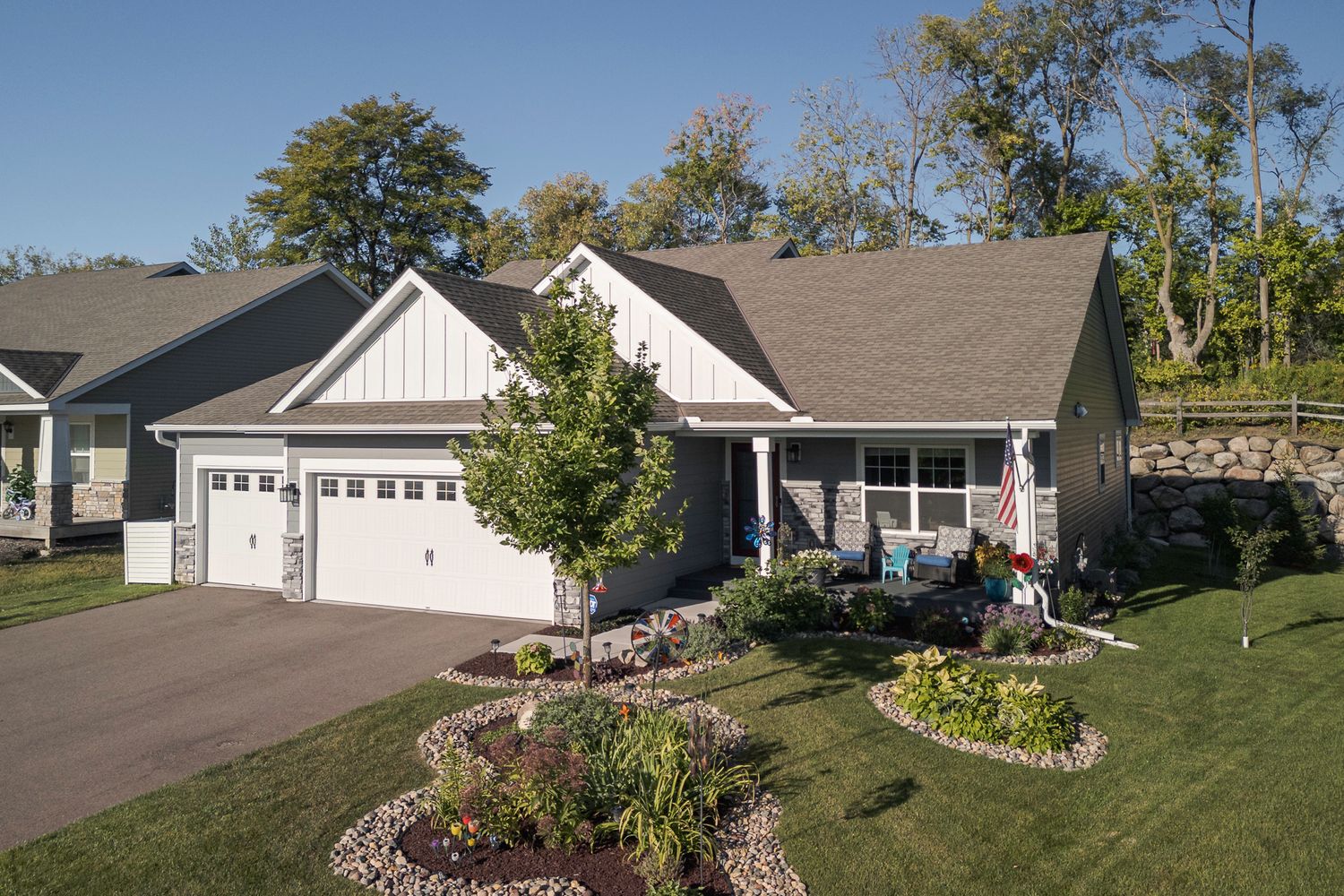 Charming craftsman-style home with white siding, two-car garage, landscaped circular driveway, and lush green lawn surrounded by trees.