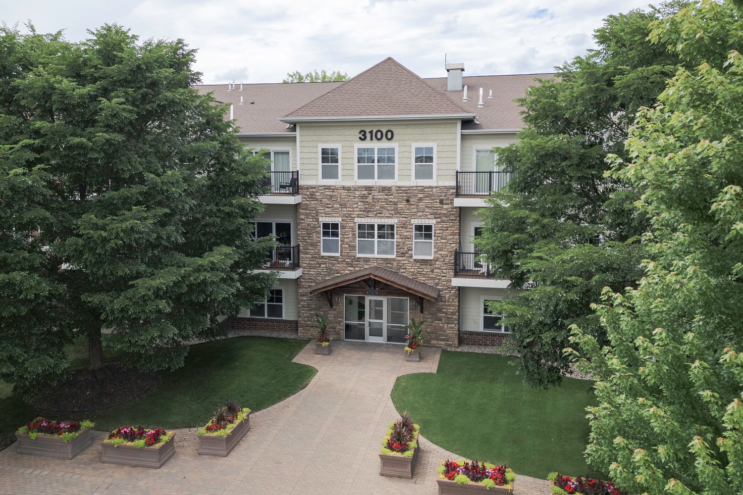 Three-story stone and siding apartment building at 3100, surrounded by mature trees and manicured landscaping.