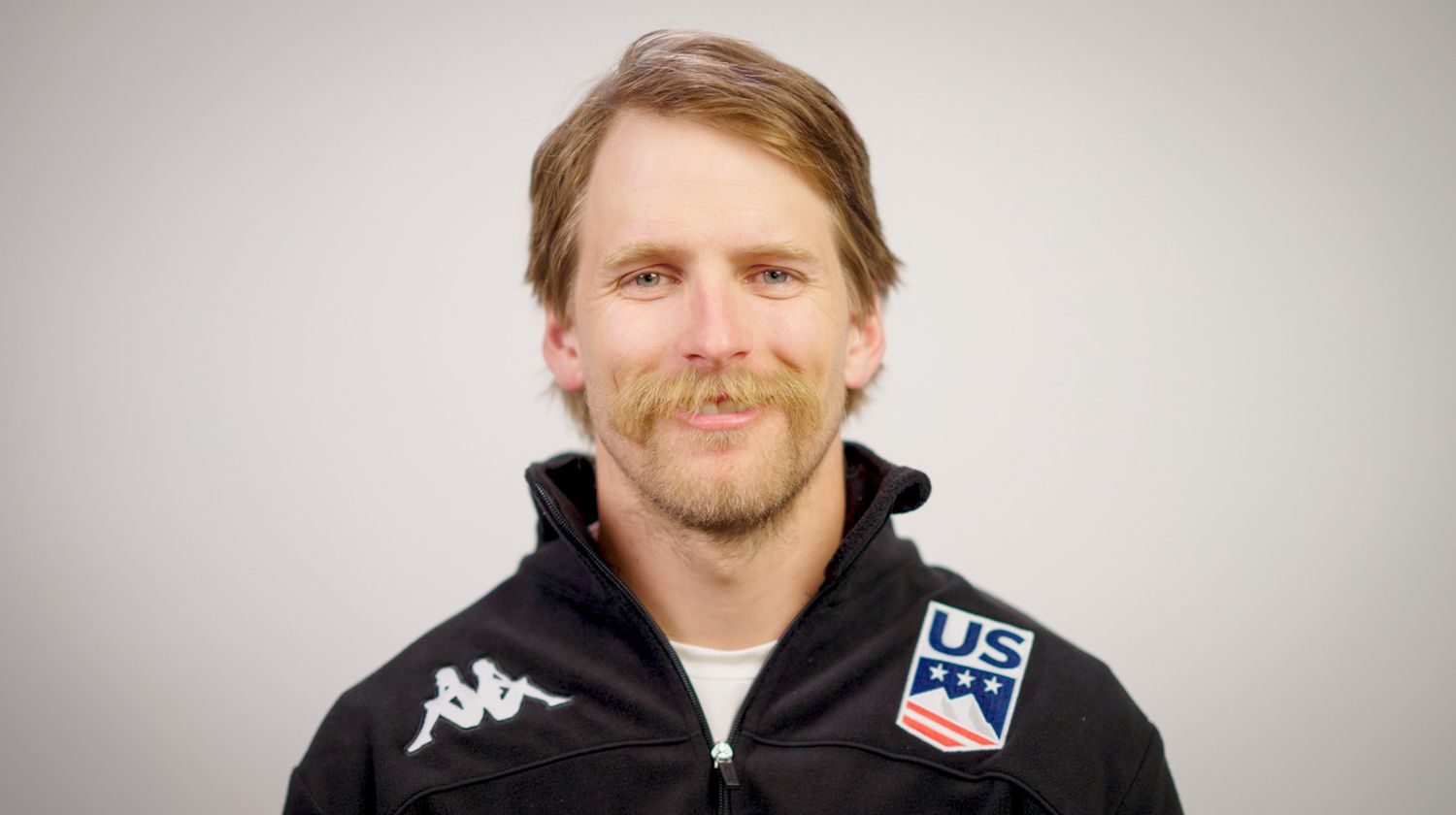 Professional headshot of athlete wearing US team jacket against white backdrop.