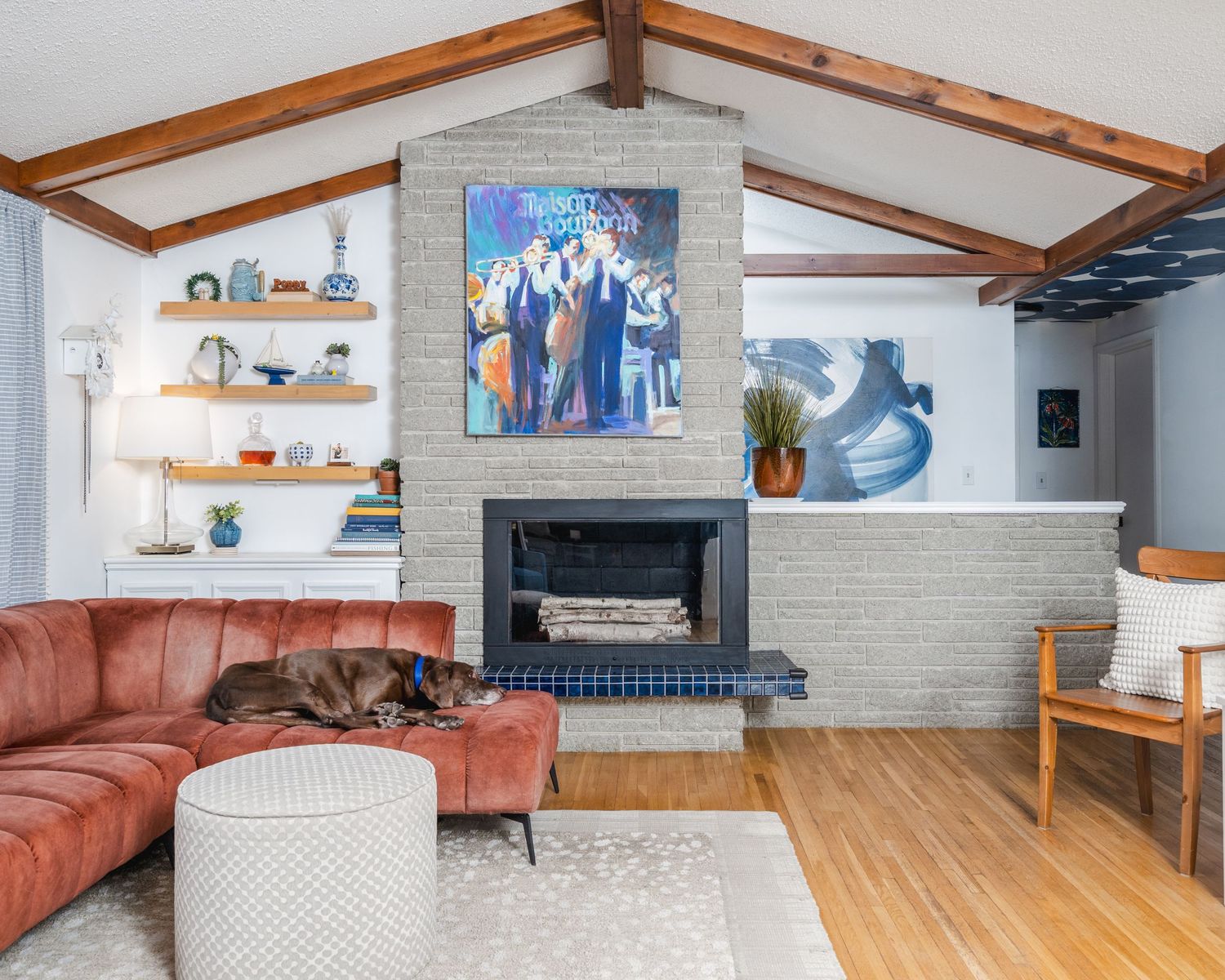 Modern living room with exposed wood beams, brick fireplace, and coral sectional sofa features hardwood floors and coastal decor.