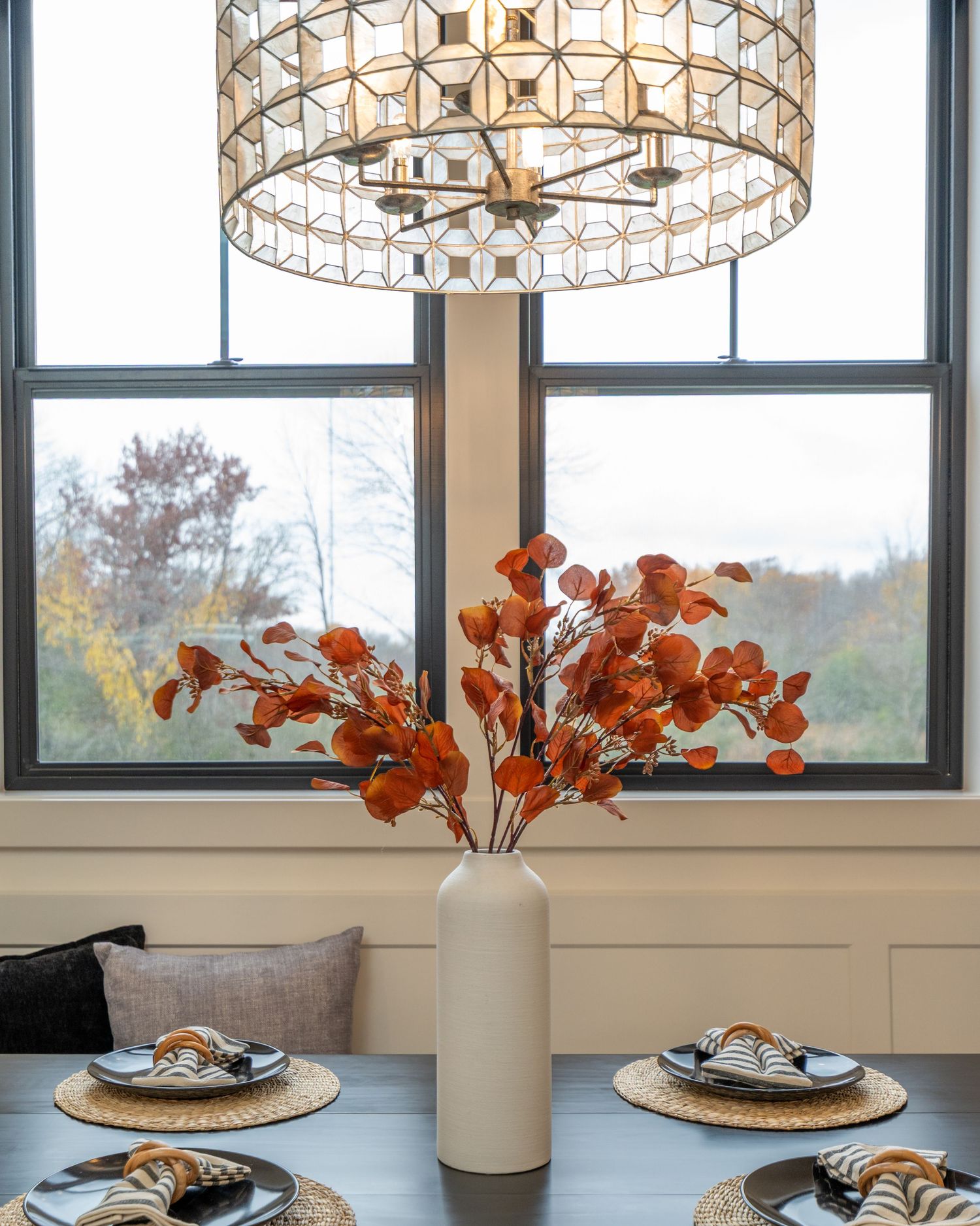 Modern dining room table with orange flowers in white vase and circular pendant lights hanging above.