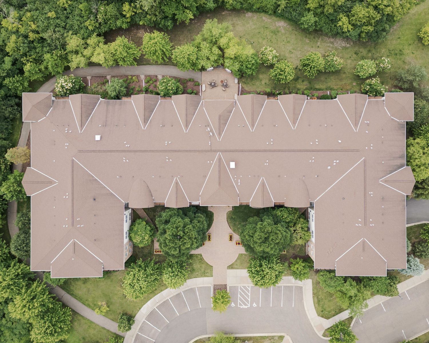 Aerial view of a large brown-roofed building surrounded by lush green trees and a parking lot.