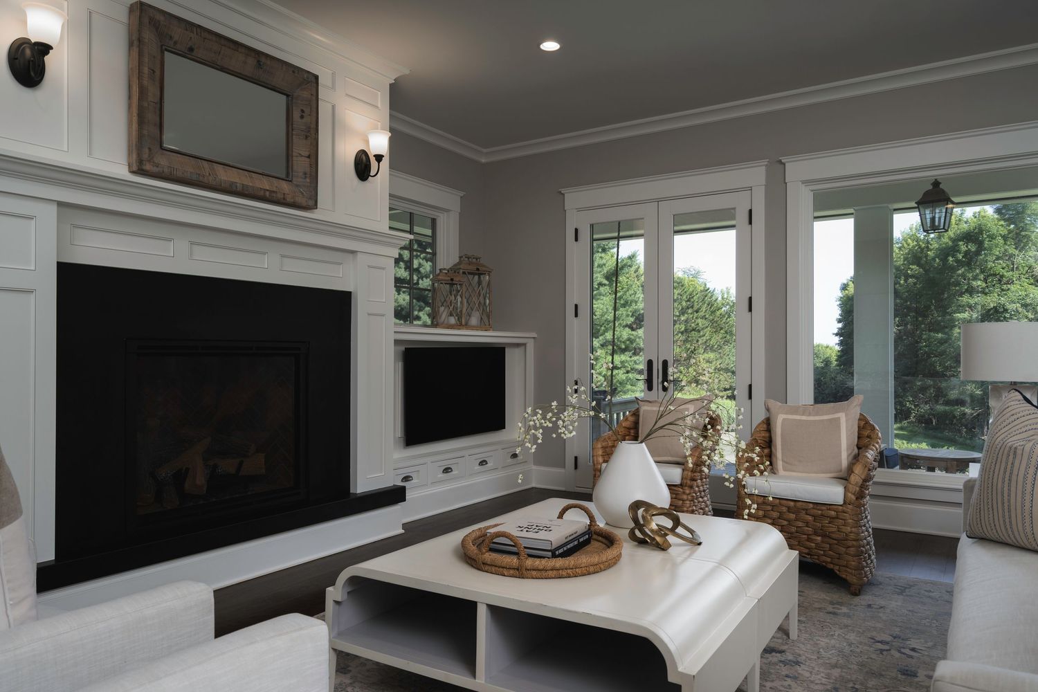 Cozy living room with white fireplace, built-in shelving, wicker chairs, and large windows with natural light.