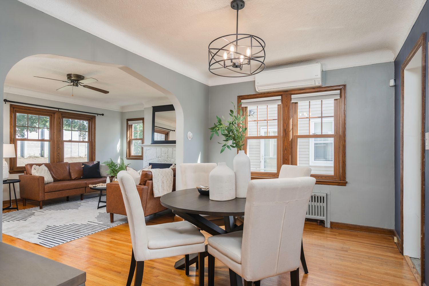 Bright dining room with round table, white chairs, hardwood floors, arched doorway, and modern chandelier.