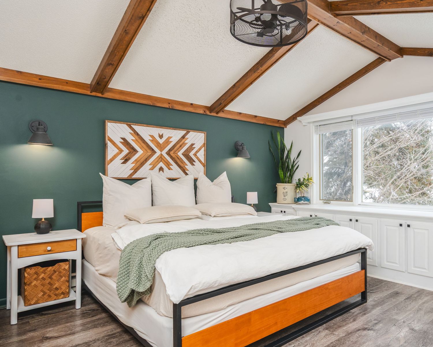 Modern bedroom with white bedding, orange accents, exposed wood beams, and teal walls in attic conversion space.