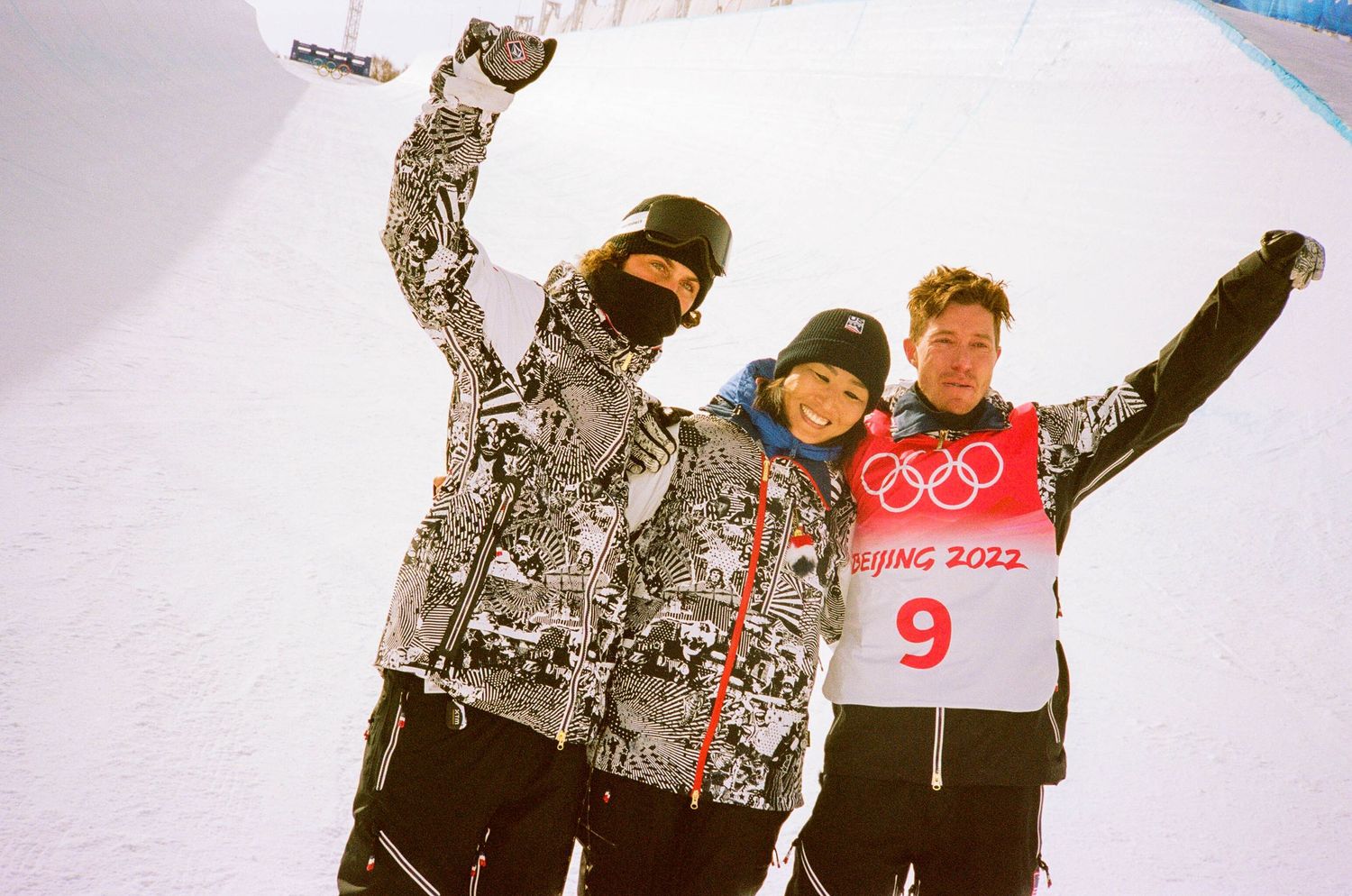Three Olympic athletes celebrating on snowy slope.