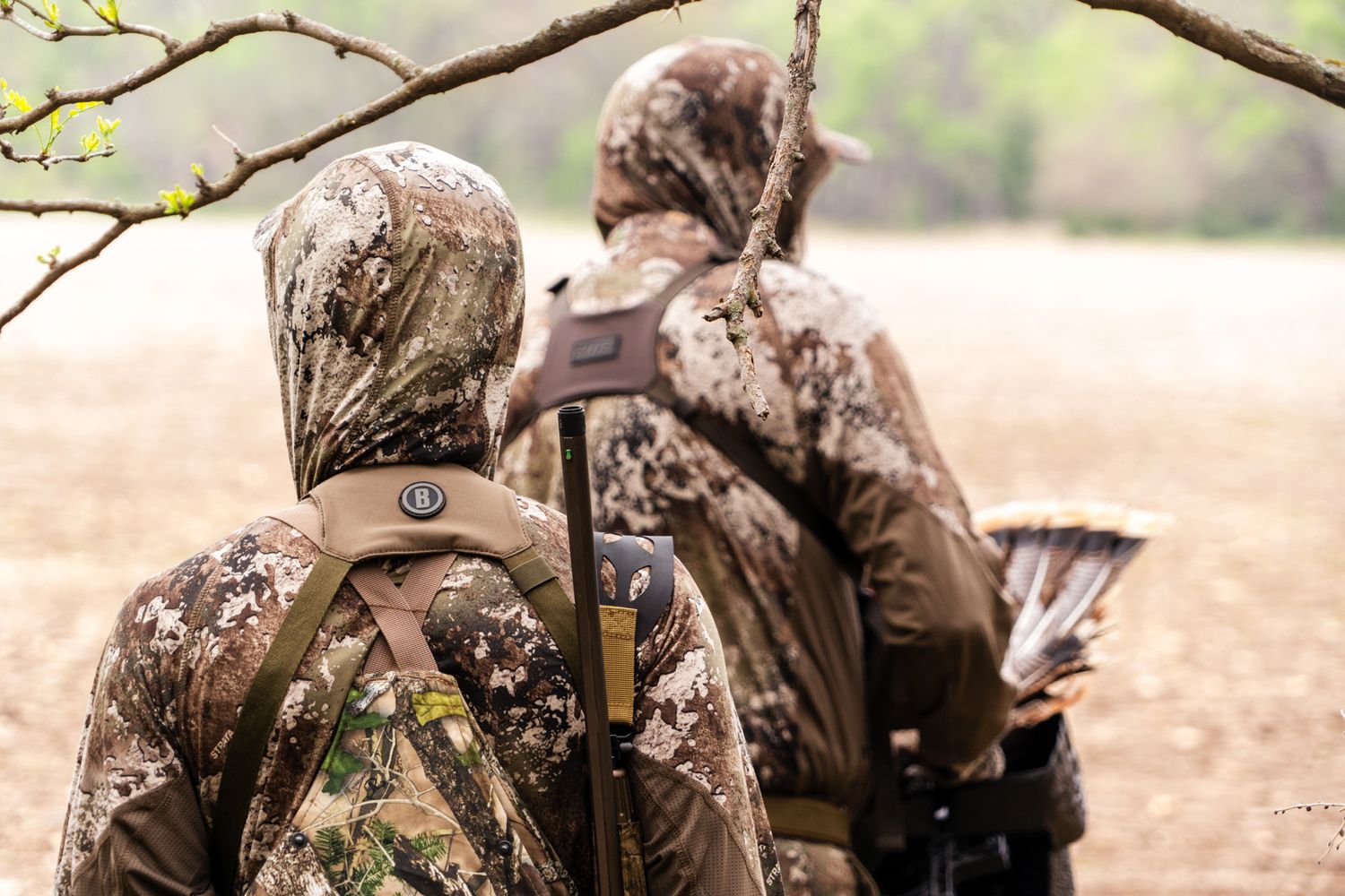 Two hunters in camouflage gear walking through a field while hunting.
