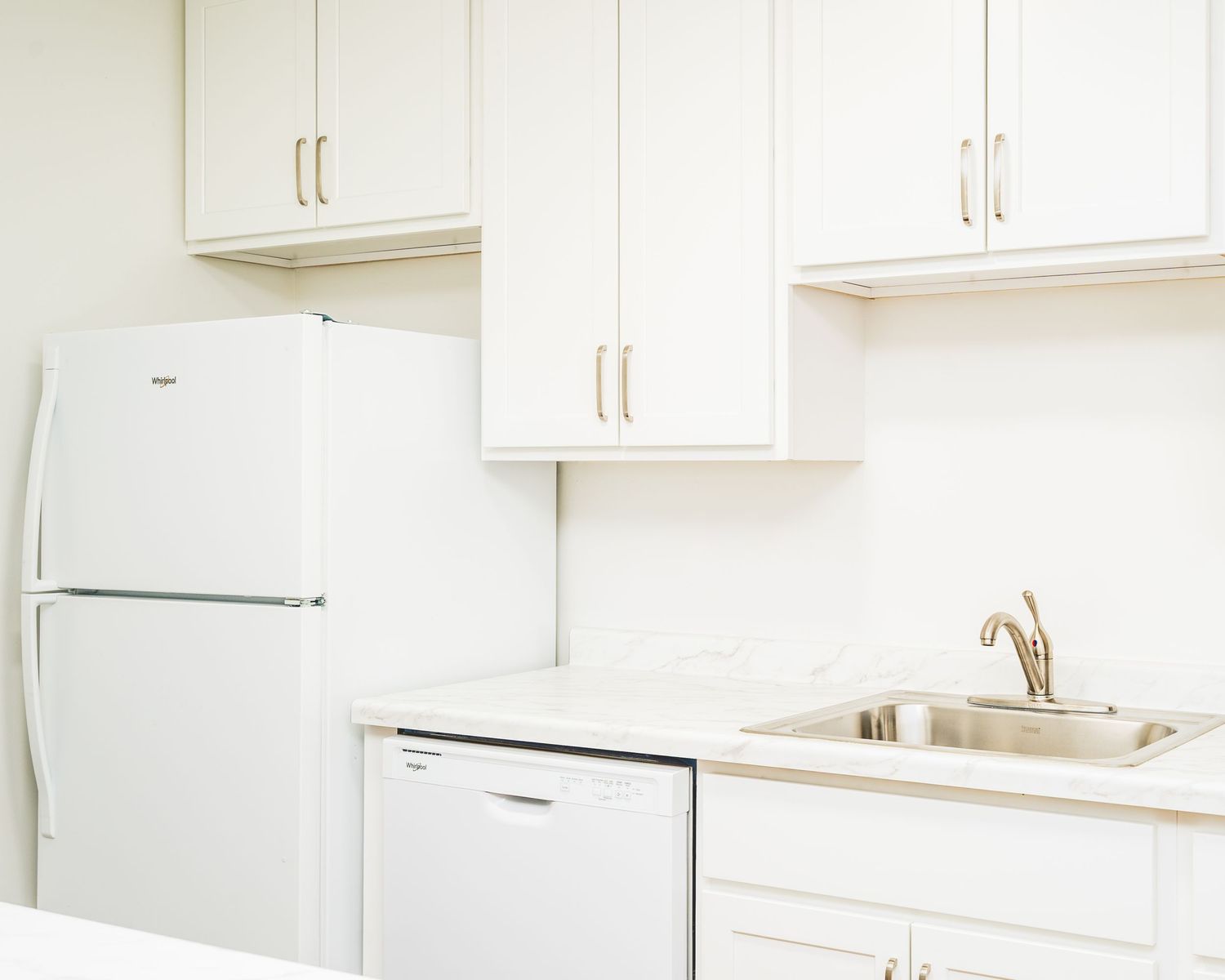 A minimalist white kitchen with white cabinets, a white refrigerator, and a dishwasher with stainless steel sink and faucet.