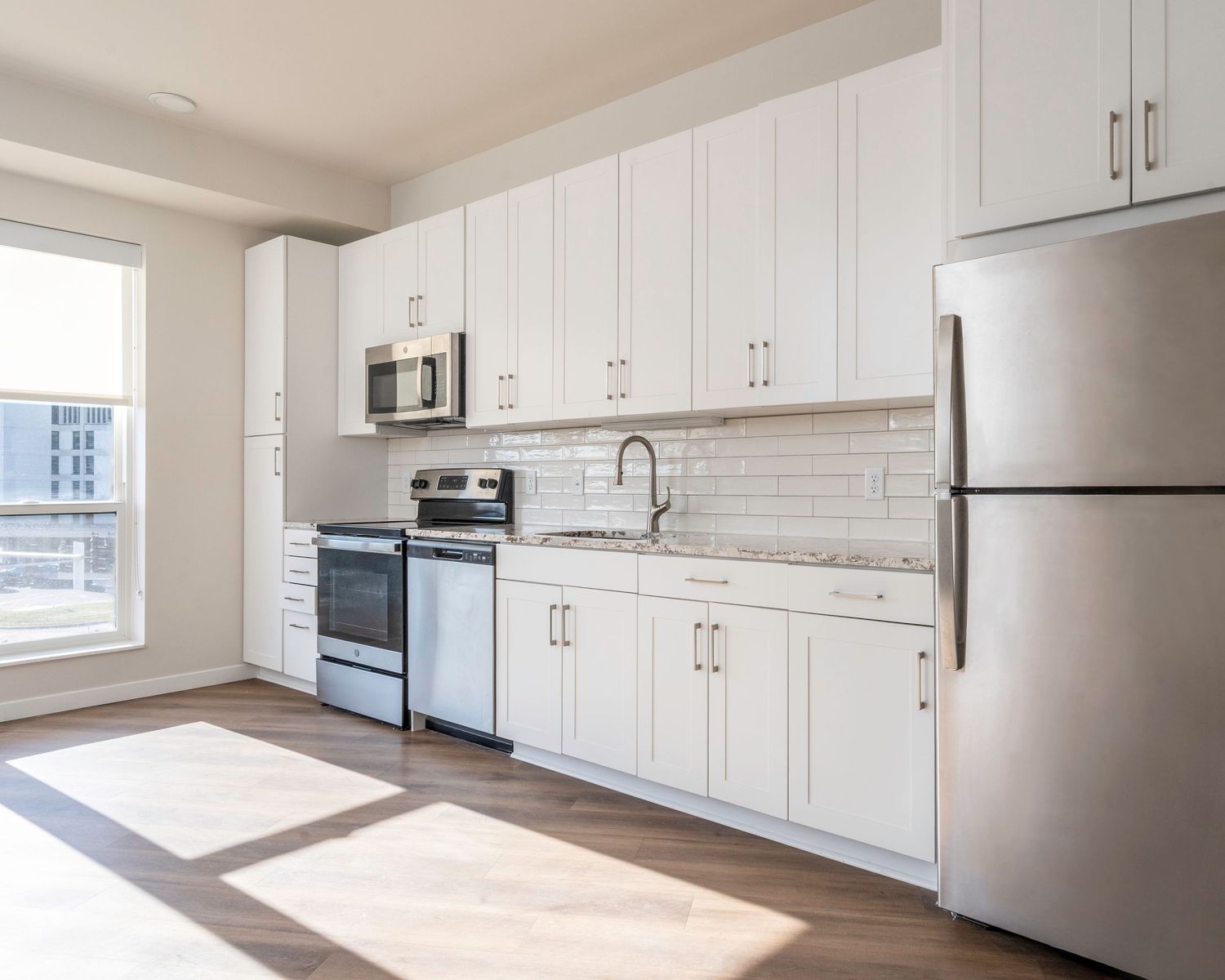 Modern kitchen with white shaker cabinets, stainless steel appliances, subway tile backsplash, and hardwood floors in bright apartment.