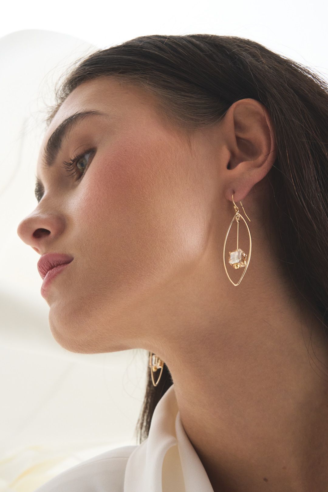 Elegant gold teardrop earring with delicate crystal detail shown in profile against soft lighting.