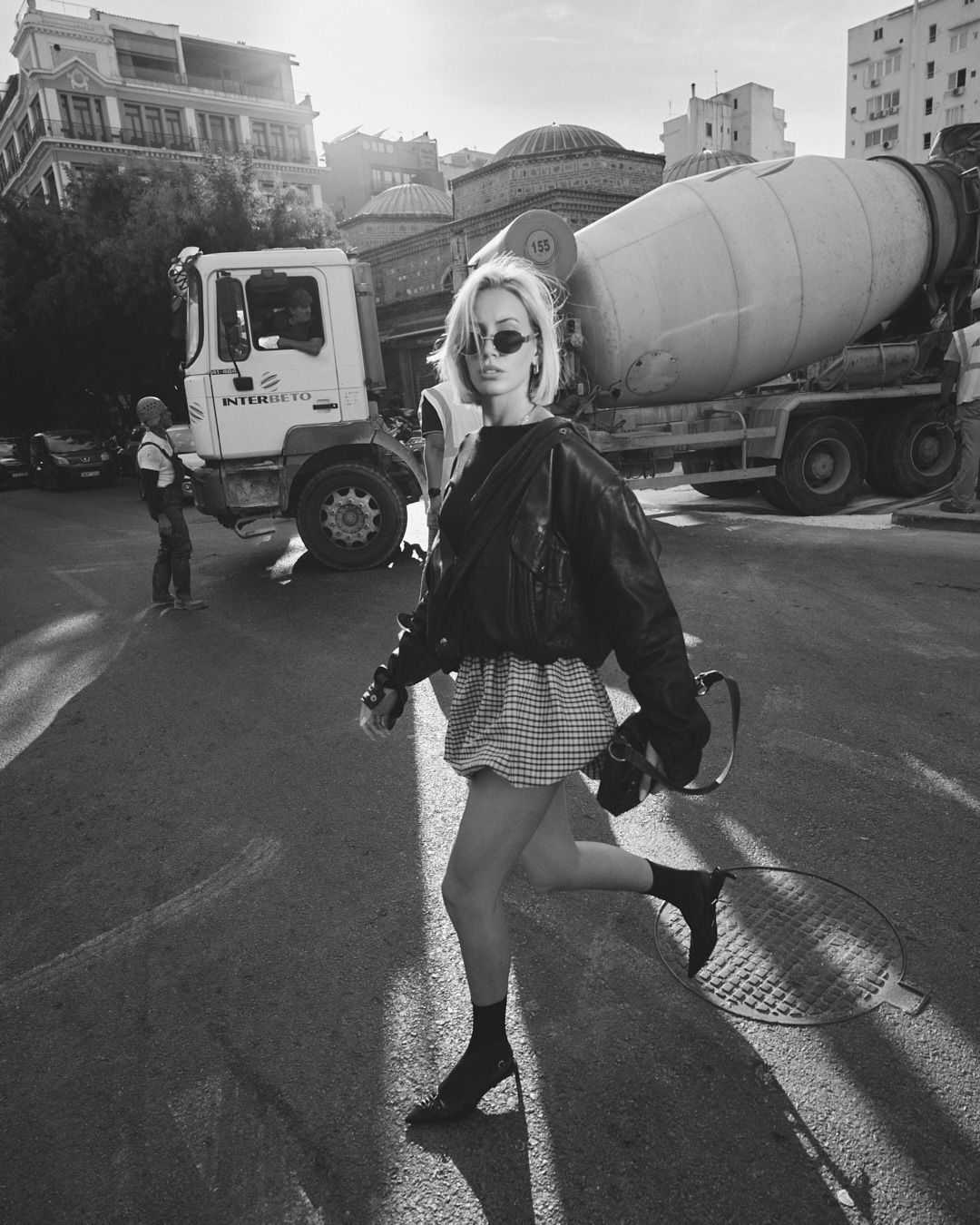 Stylish black and white street scene with a fashionable figure posing in front of a cement mixer truck.
