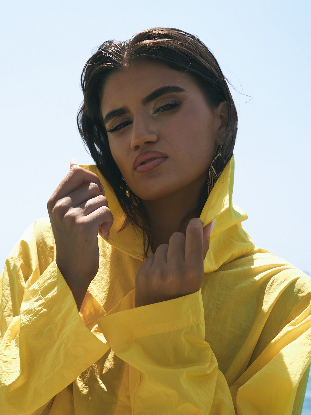 Woman in yellow raincoat pulling up hood outdoors.