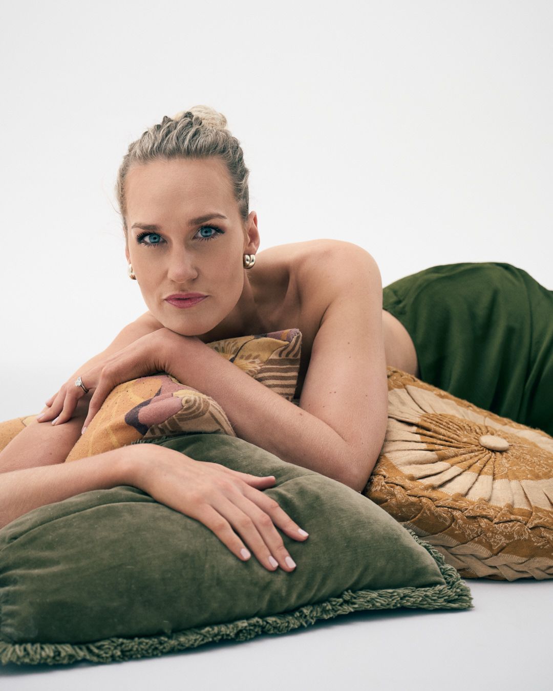 A person reclines on a green velvet couch with a gold pillow in an artistic boudoir photoshoot.