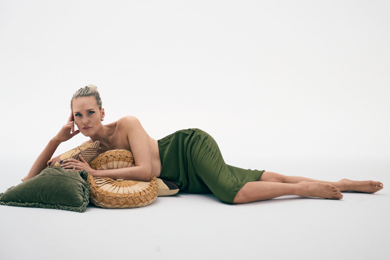 Person in green loungewear relaxes on floor with woven rattan pillow against white background.