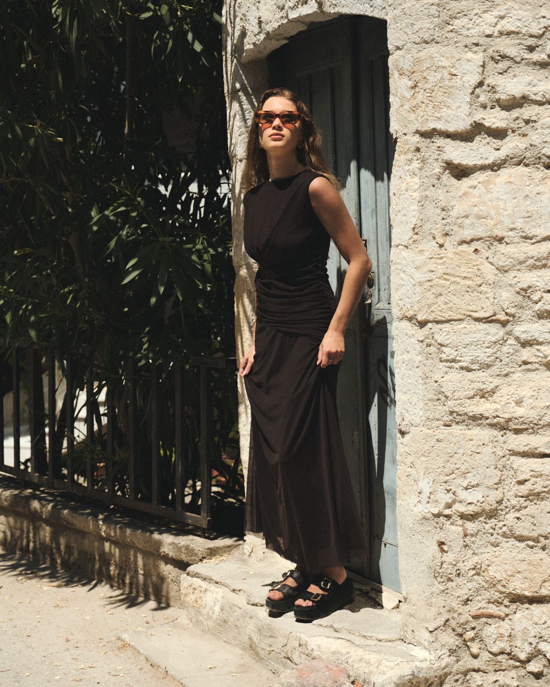 A series of fashion photos showing a black summer dress styled against a white stone wall in natural lighting.