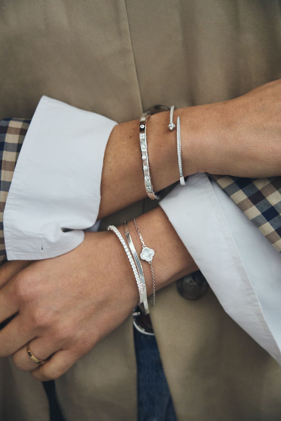 Multiple silver bracelets and bangles stacked on wrist with white sleeve detail.