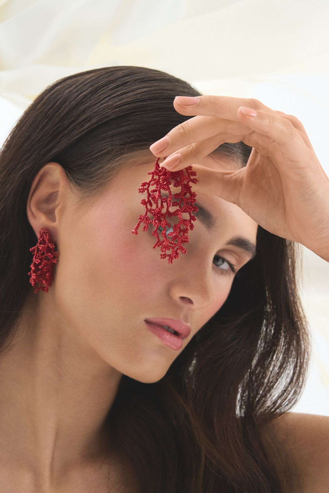Striking red coral-inspired statement earrings styled with natural makeup and dark hair.