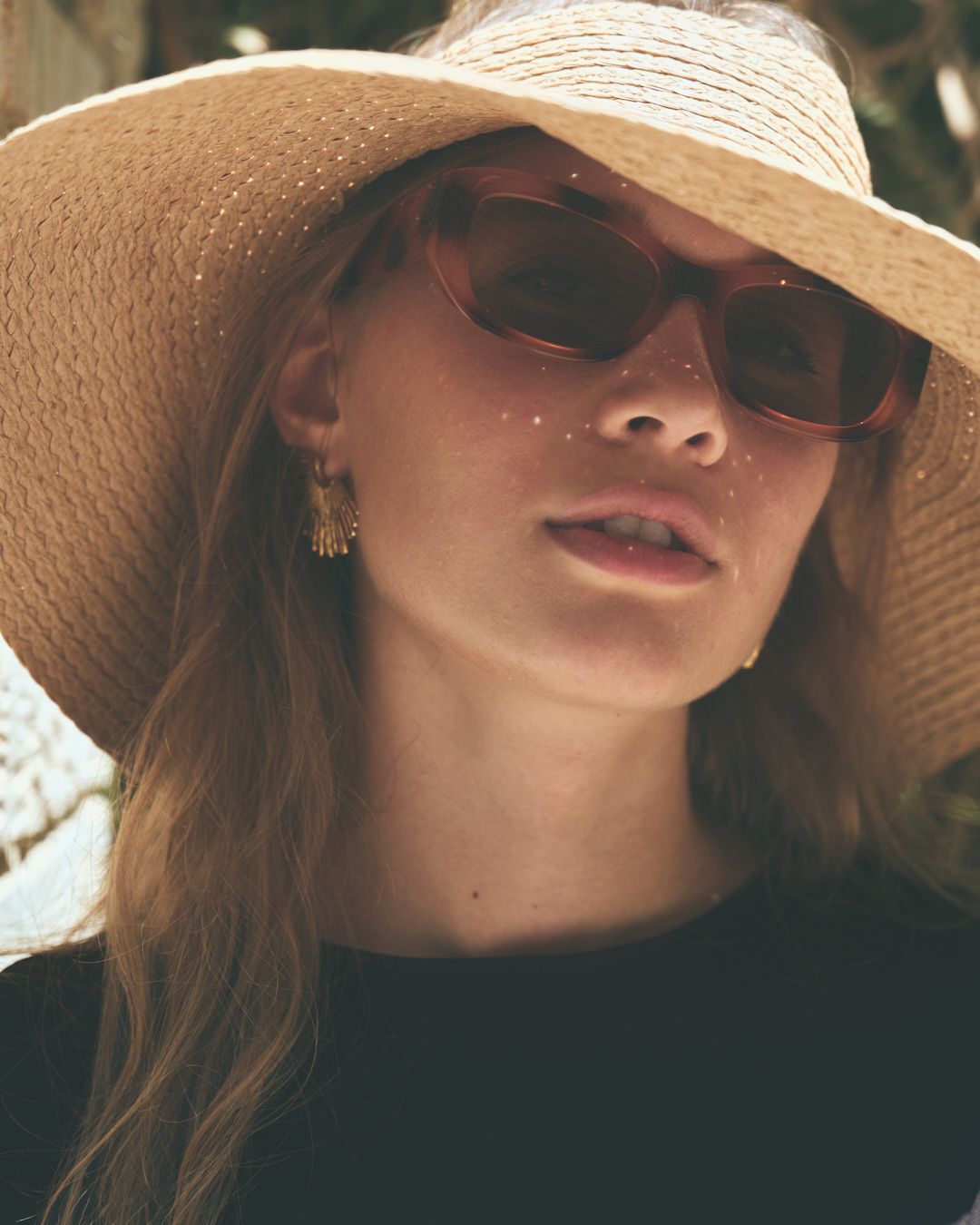 Closeup of a woman wearing a straw sun hat and sunglasses in warm natural lighting.