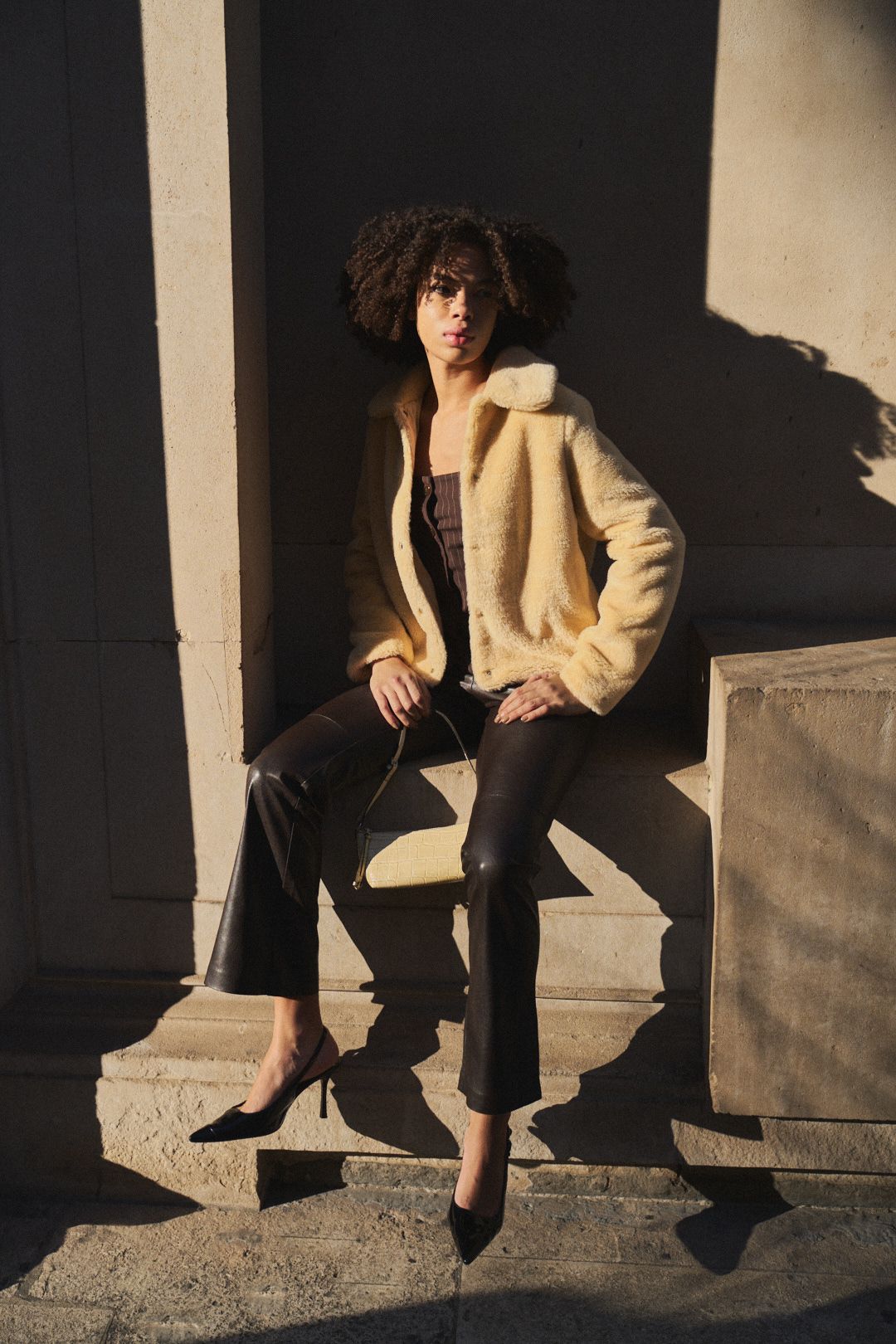 Artistic fashion photo series showing legs in black pants and beige jacket sitting on stone steps in dramatic lighting.