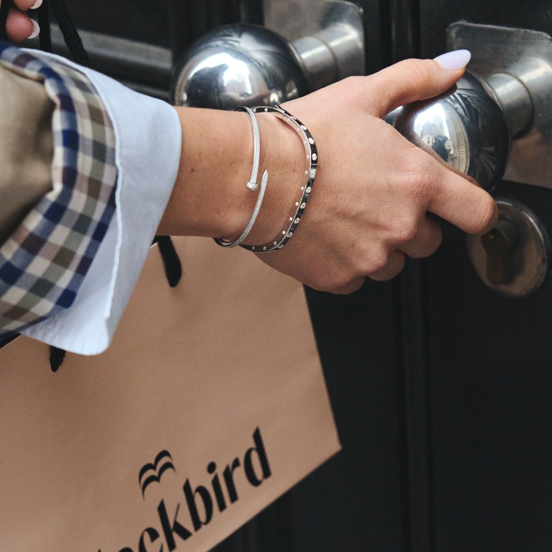 Hand wearing silver bracelet reaching for black shopping bag handle.