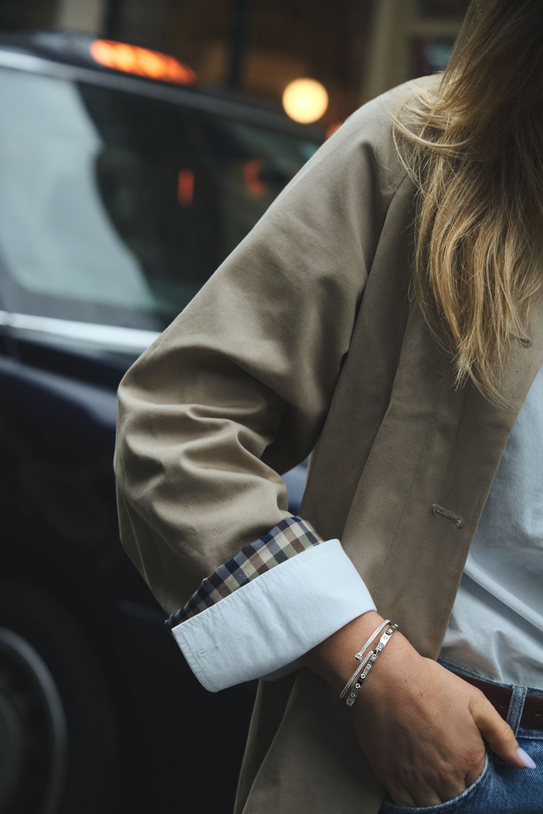 Person in beige blazer and plaid shirt showing silver bracelet detail.